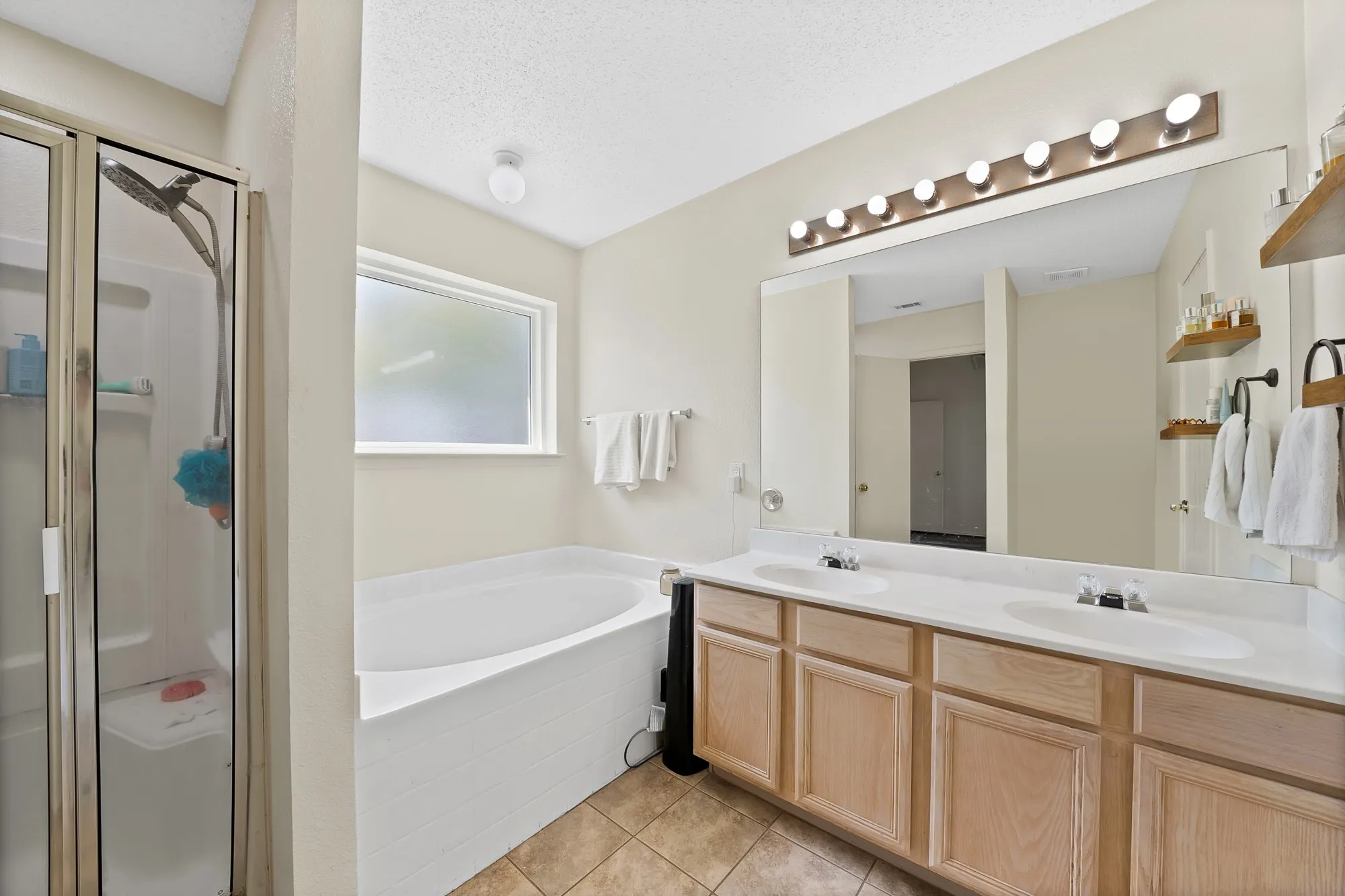 Dual vanity with integrated sinks, large wall-mounted mirror, light wood-finish cabinetry, and tiled flooring