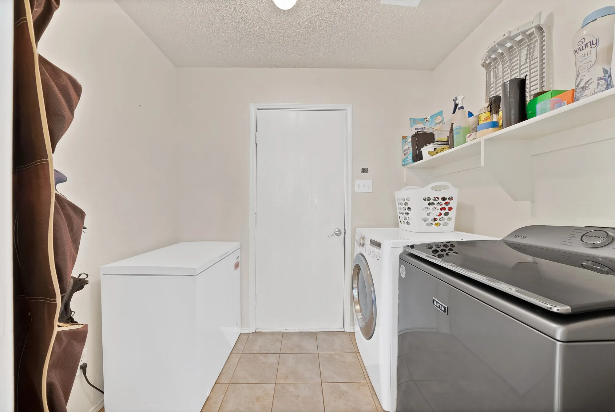 Laundry area featuring tiled flooring, built-in shelving, and a solid core door