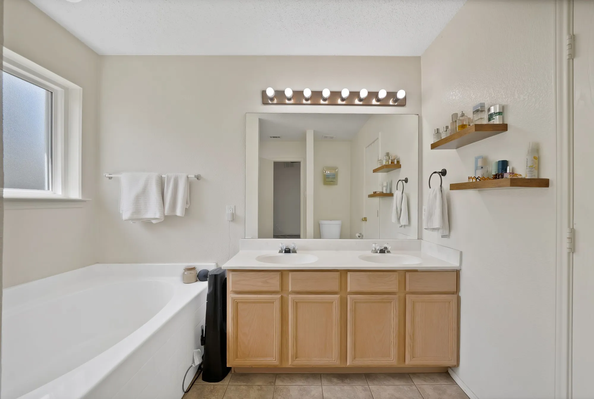 Dual vanity with a laminate countertop, light wood-finish cabinetry, and an integrated bathtub