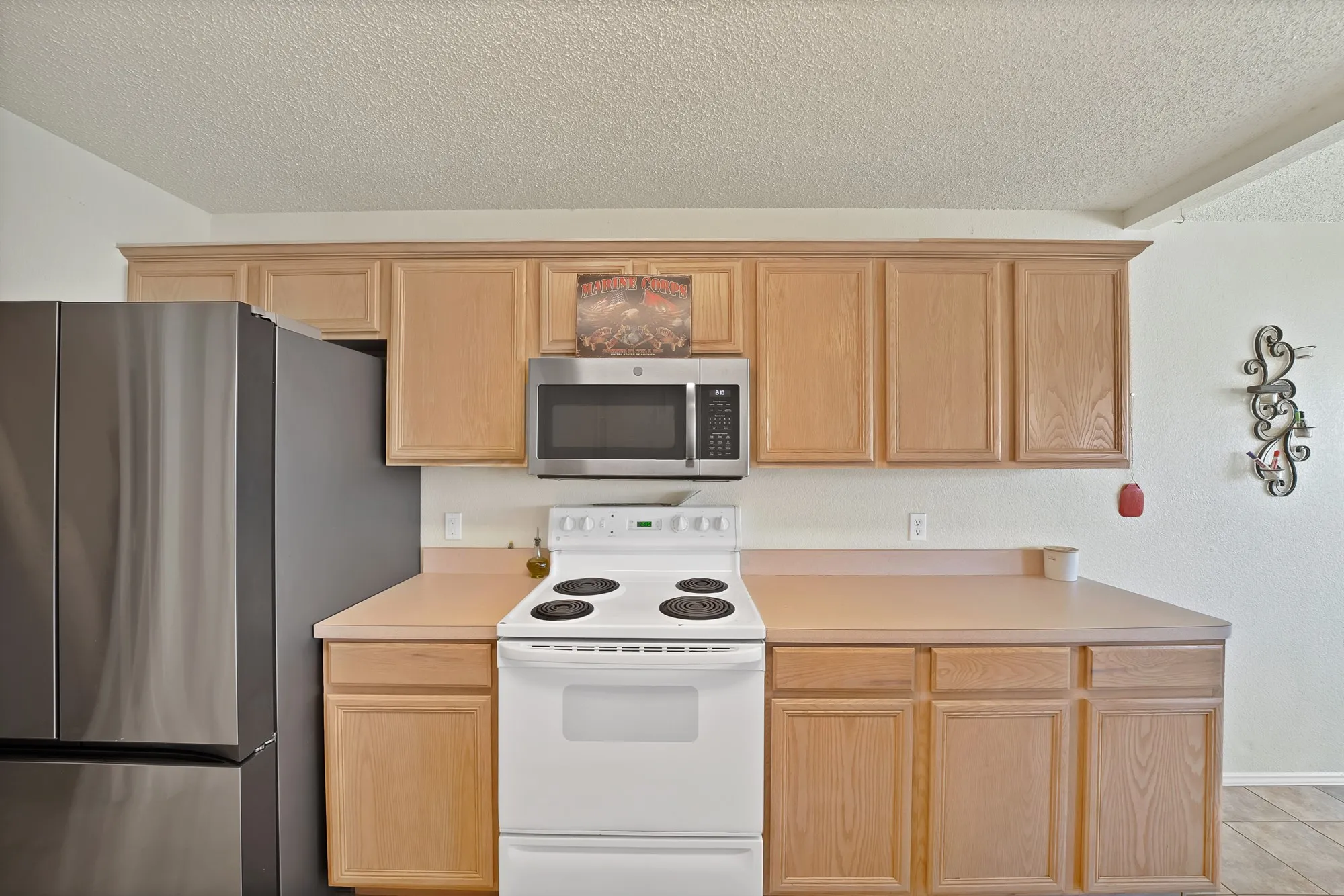 Kitchen featuring light wood-finish cabinetry, solid surface countertops, a stainless steel refrigerator, a white electric range, and a stainless steel over-the-range microwave