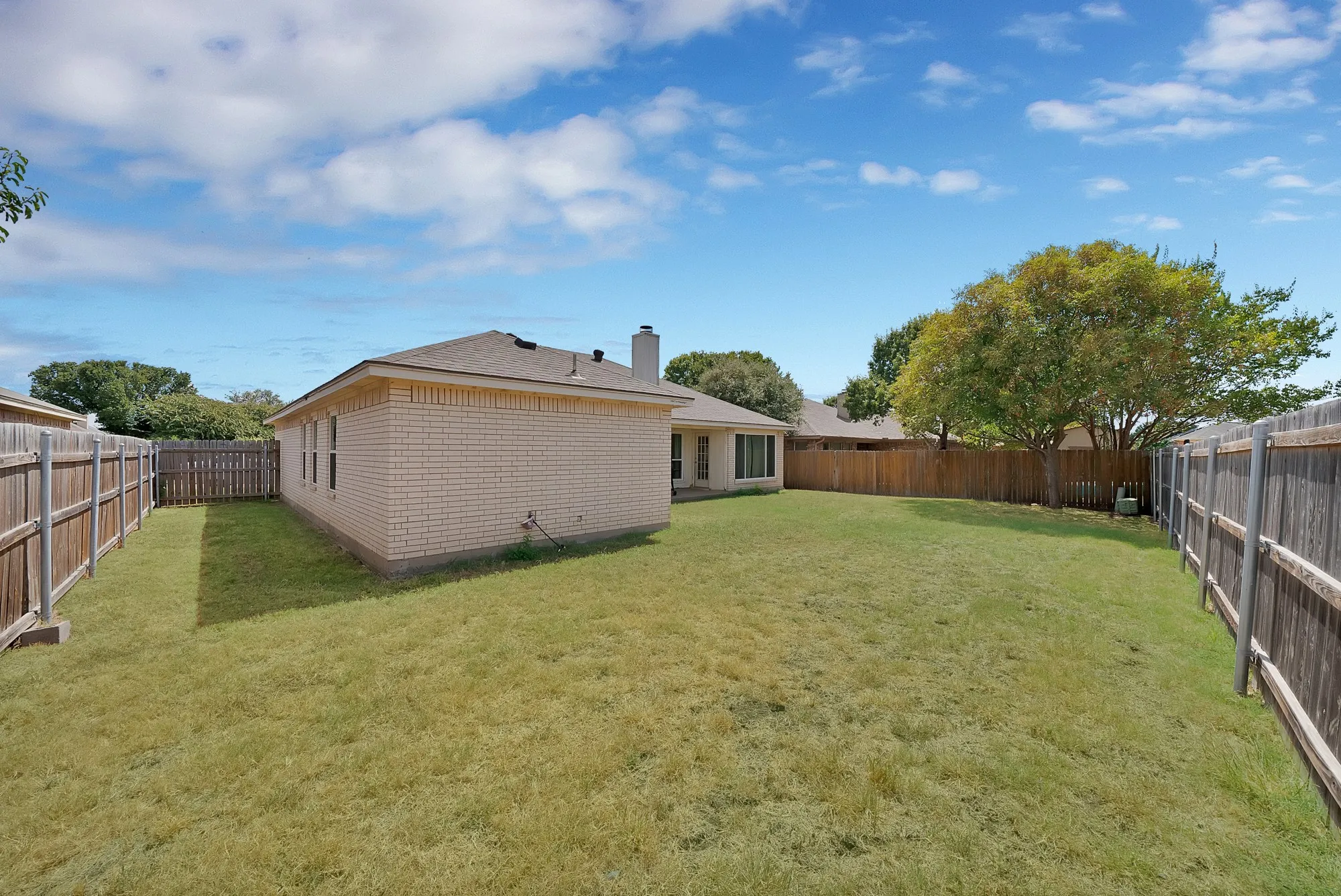 Expansive backyard featuring a manicured lawn, full perimeter privacy fencing, and mature trees