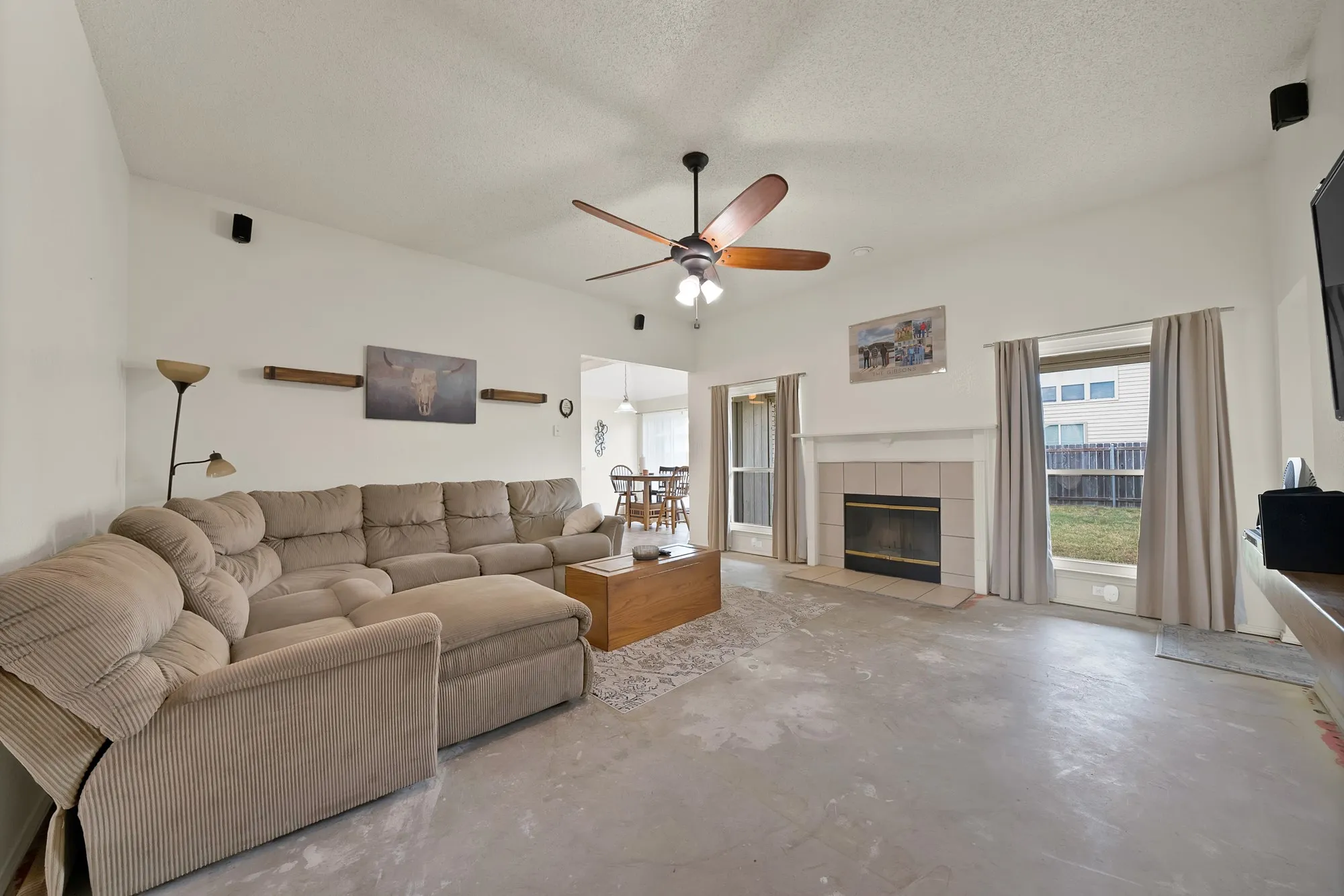 Vaulted ceiling with a ceiling fan, a fireplace with a tiled surround, and two sets of glass patio doors providing exterior access