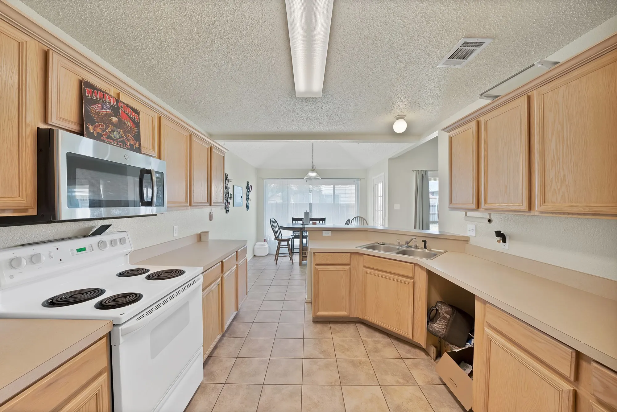 Galley kitchen featuring wood-finish cabinetry, tile flooring, and a stainless steel microwave