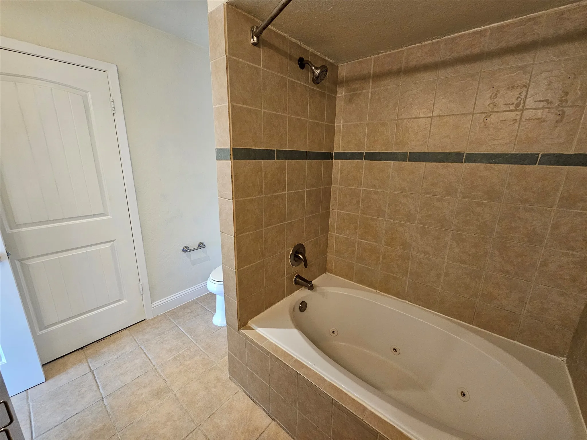 Built-in jetted tub with tiled surround, tile flooring, and a white paneled door