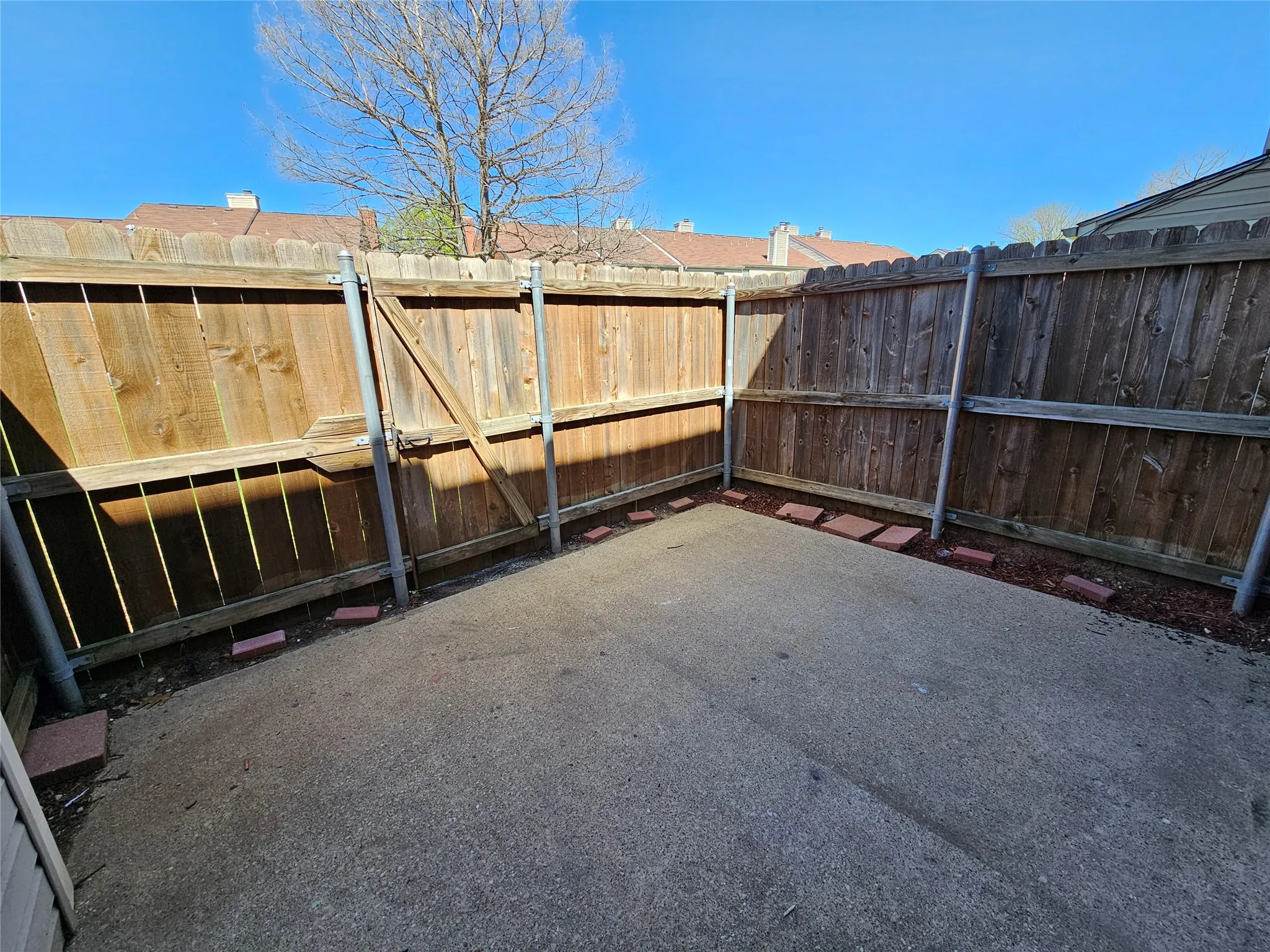 Private concrete patio with wood fencing, a wood gate, and landscape edging