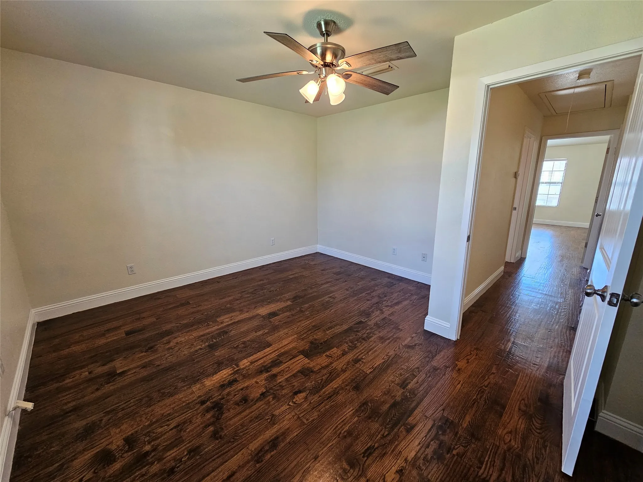 Wood-finish flooring, ceiling fan with integrated lighting, neutral wall paint, white trim, and a white interior door