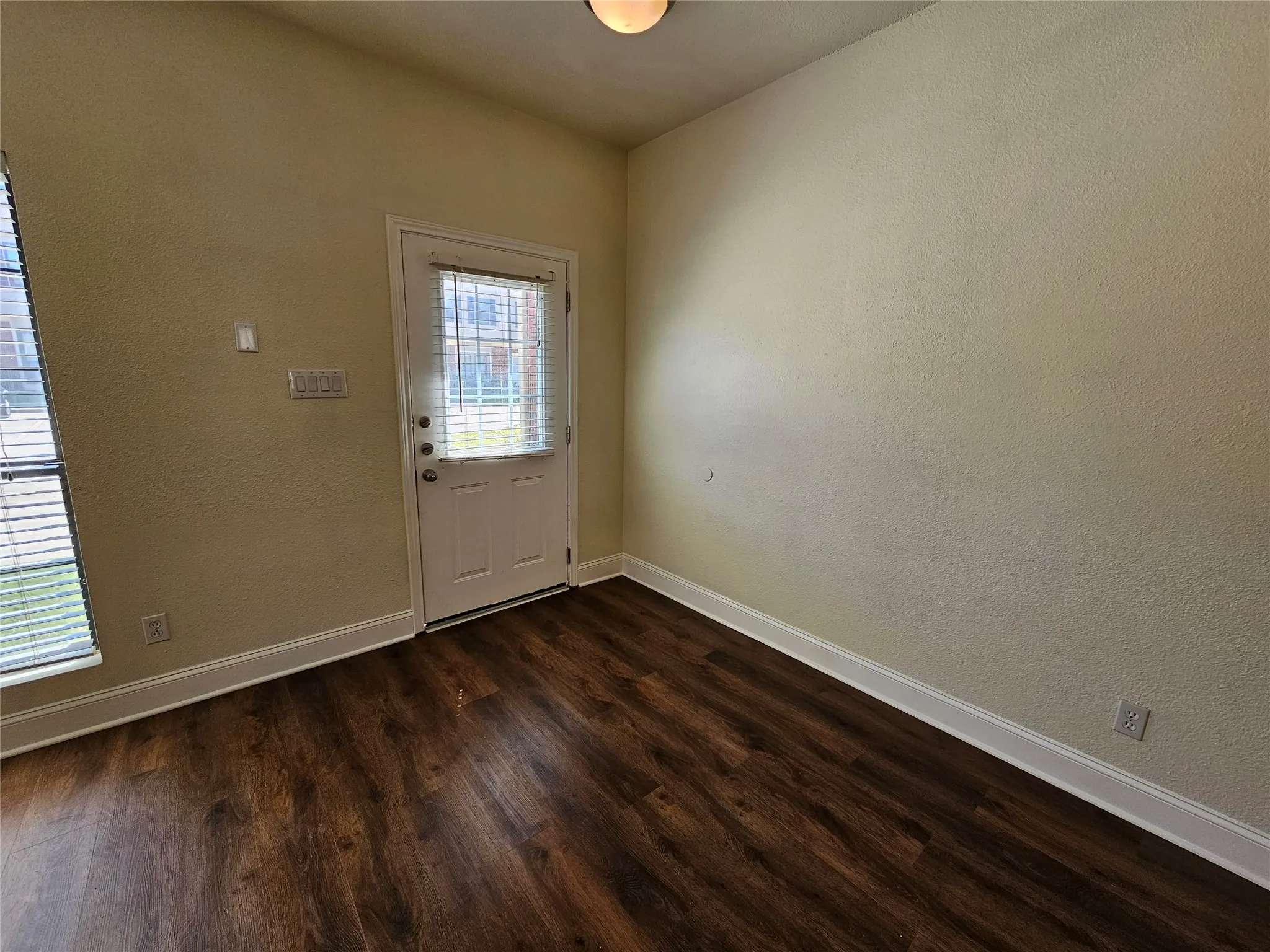 Wood-finish flooring, white trim, and a white paneled door with a privacy glass insert