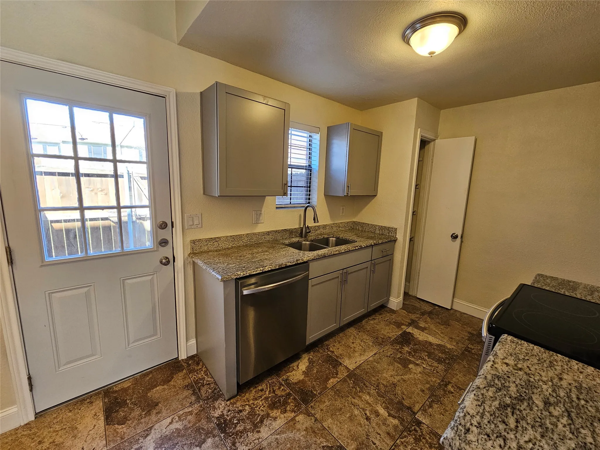 Tile flooring, light-toned cabinetry, granite-style countertops, stainless steel dishwasher, and a glass-paneled door