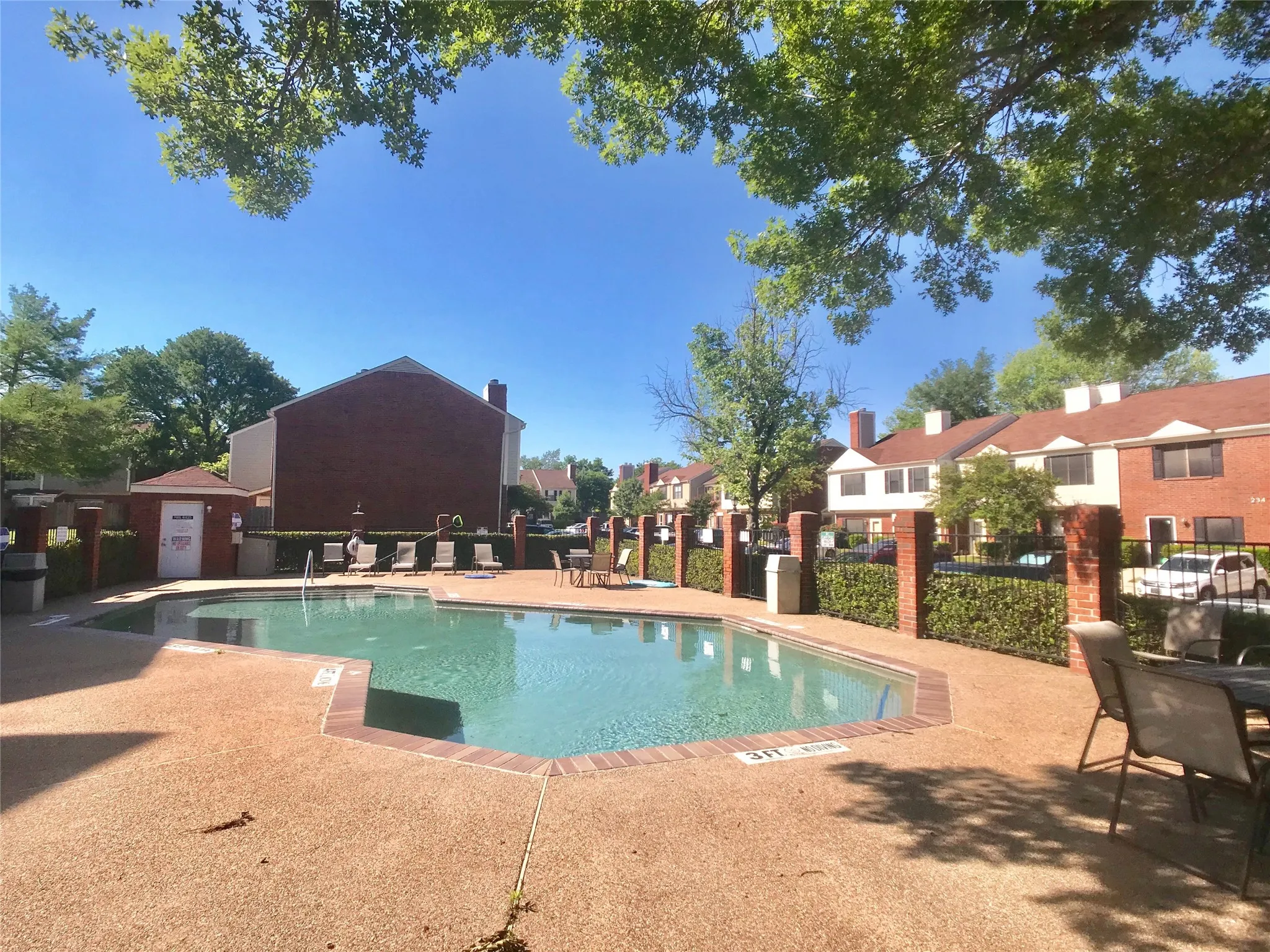 Swimming pool with a textured deck, surrounded by mature trees and brick fencing