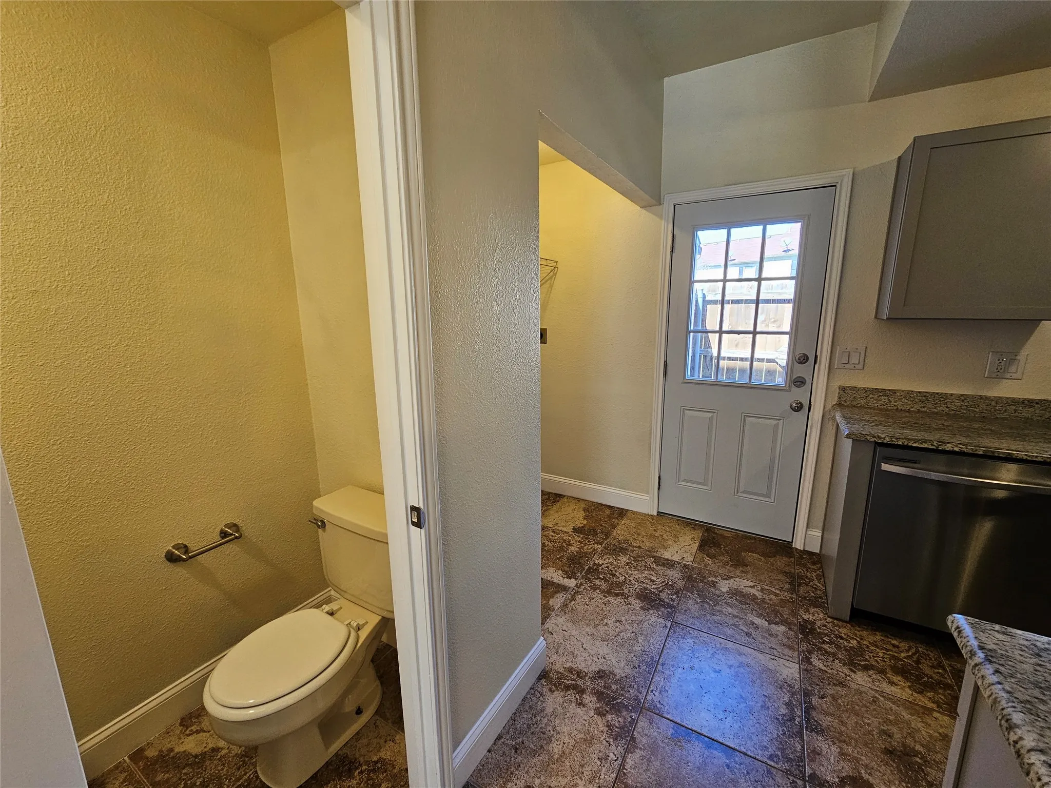 Tiled flooring throughout, featuring a white paneled door with window panes, a stainless steel appliance, and stone countertops