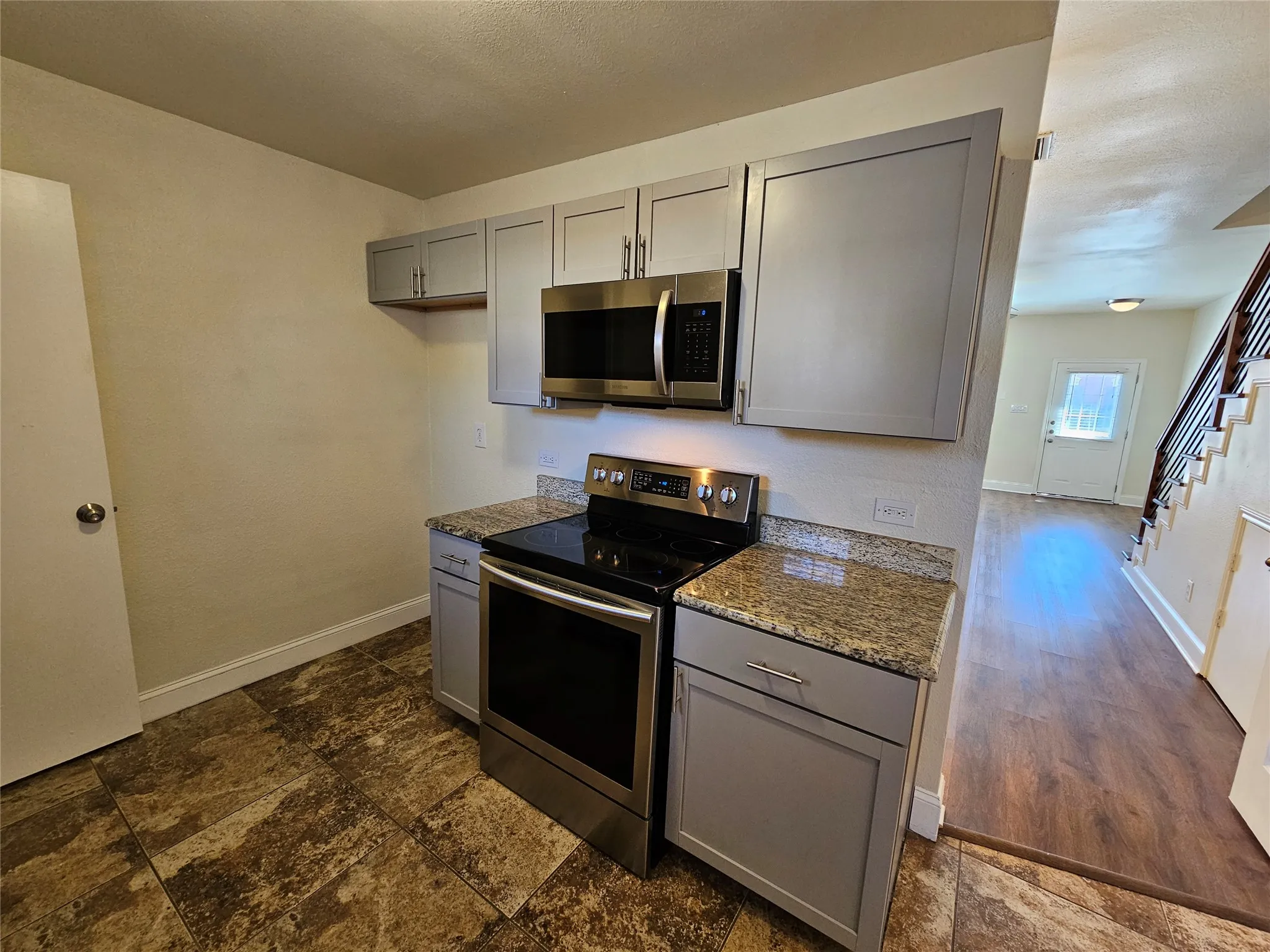 Stainless steel range and microwave, light gray cabinetry, granite countertops, and patterned floor tiles