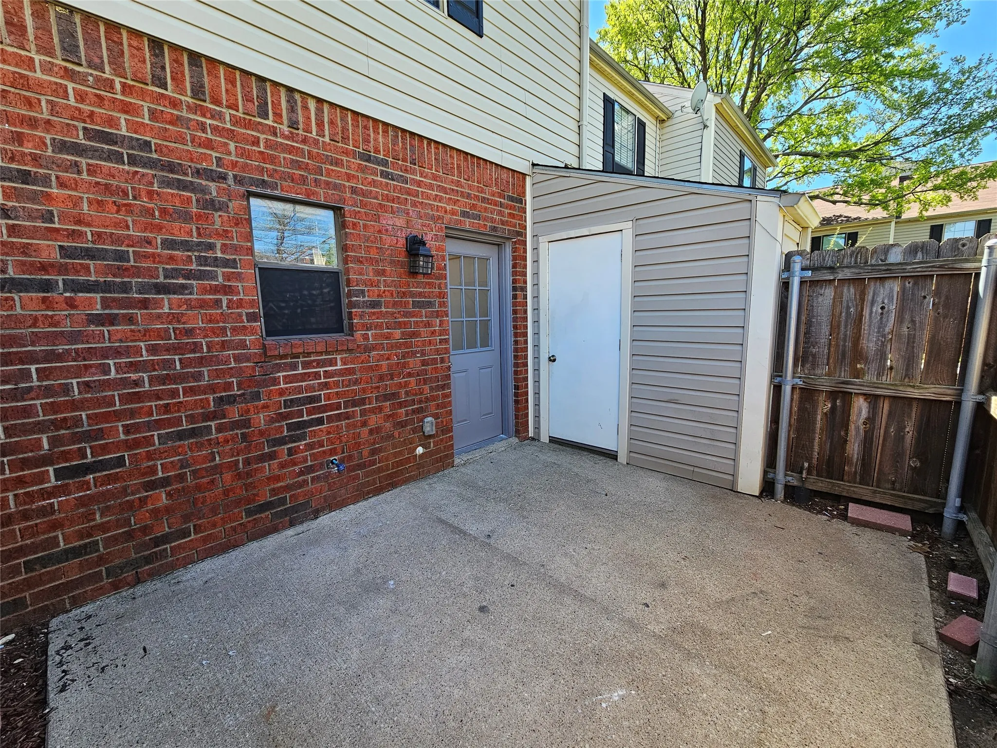 Brick exterior with a concrete patio, featuring an attached storage shed with siding
