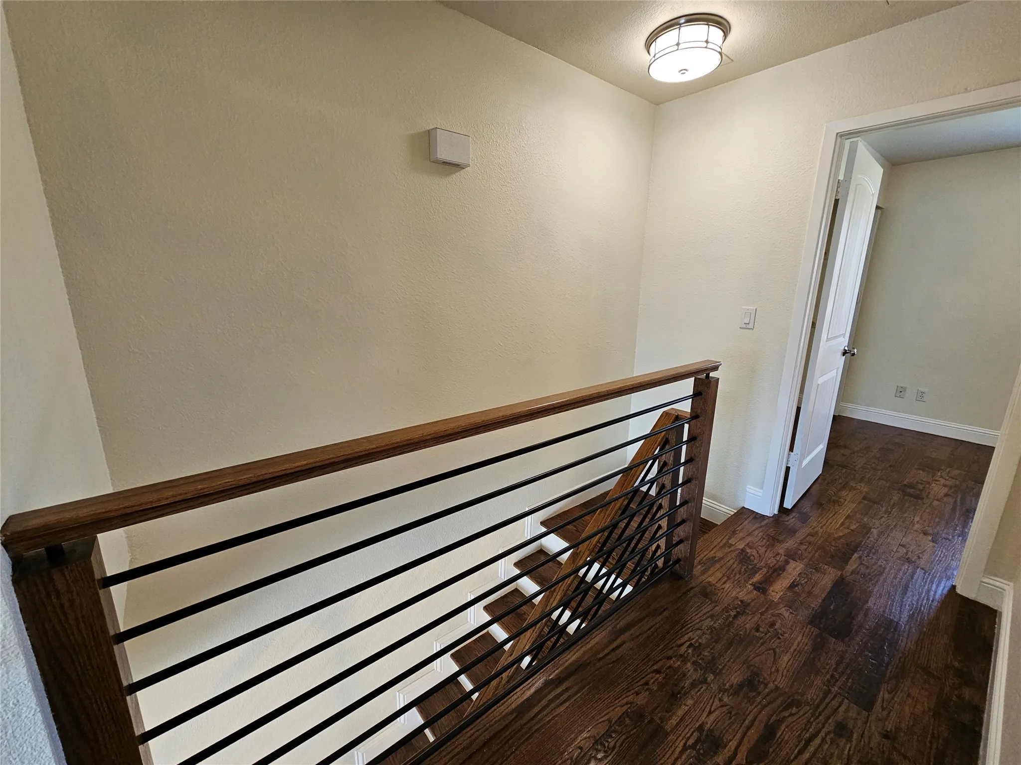 Hardwood flooring extending throughout, contemporary metal and wood railing, and a flush-mount ceiling light fixture