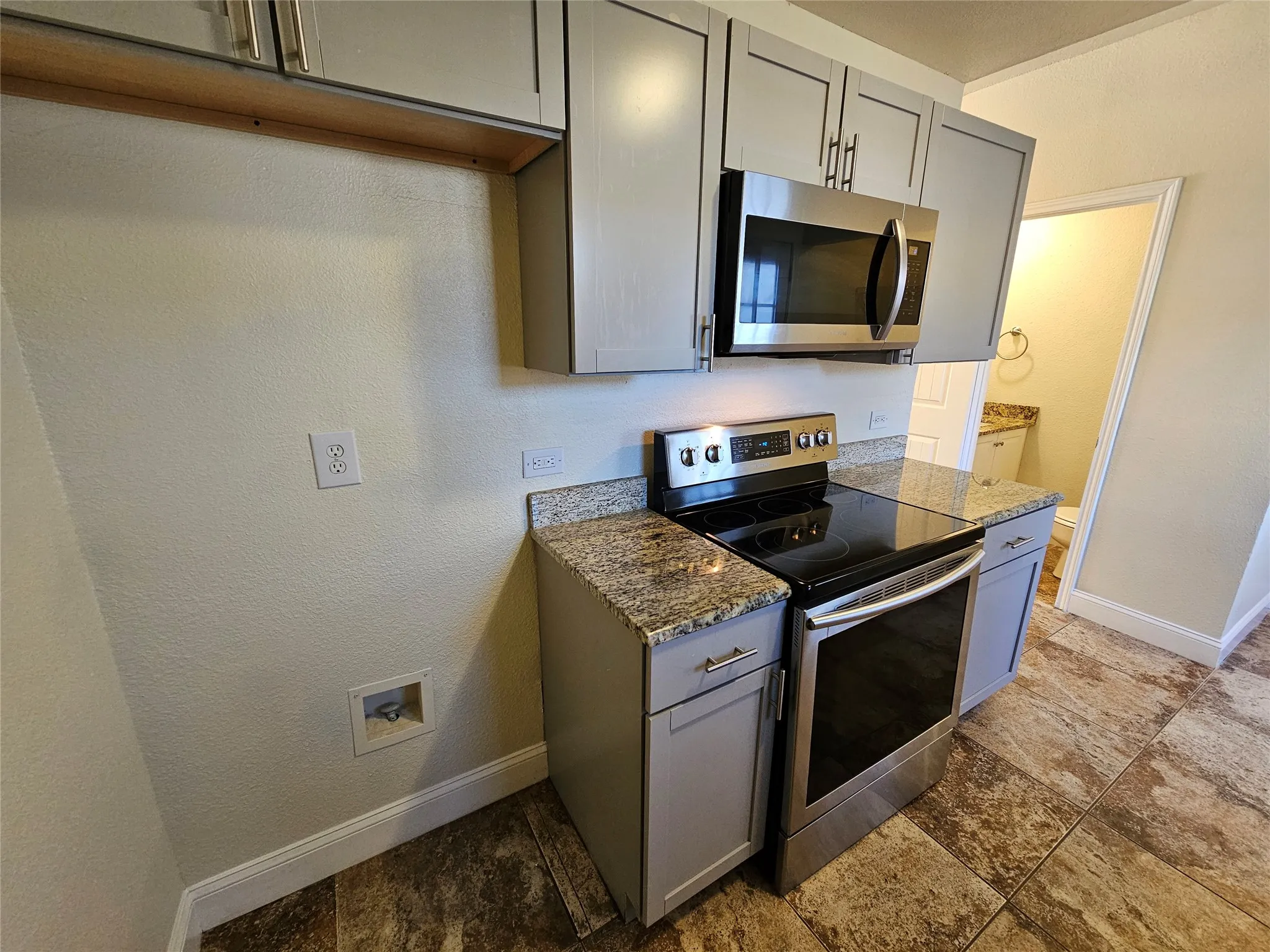 Stainless steel microwave, electric range, and granite countertops complement the gray cabinetry