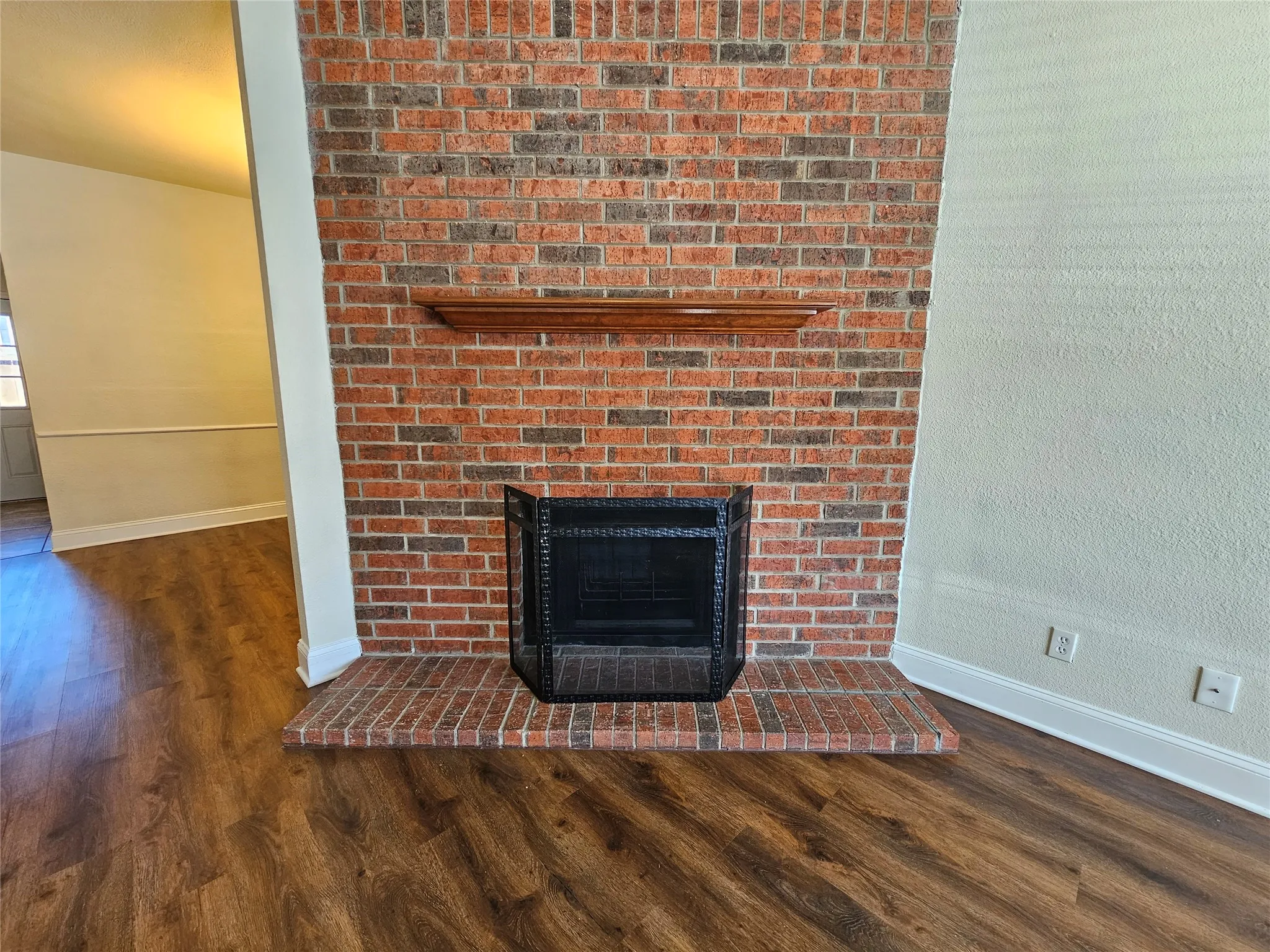 Brick-clad fireplace with a wood mantelpiece and hearth, featuring wood-finish flooring