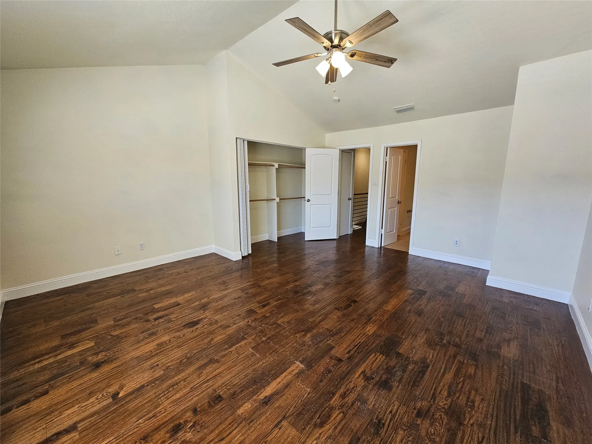 Vaulted ceiling with a ceiling fan, wood-finish flooring, and built-in closet shelving