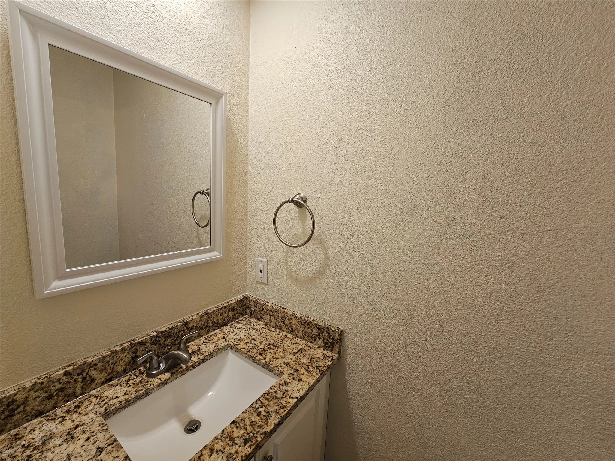 Vanity with an integrated rectangular sink, granite countertop, wall-mounted mirror with a white frame, and brushed nickel fixtures