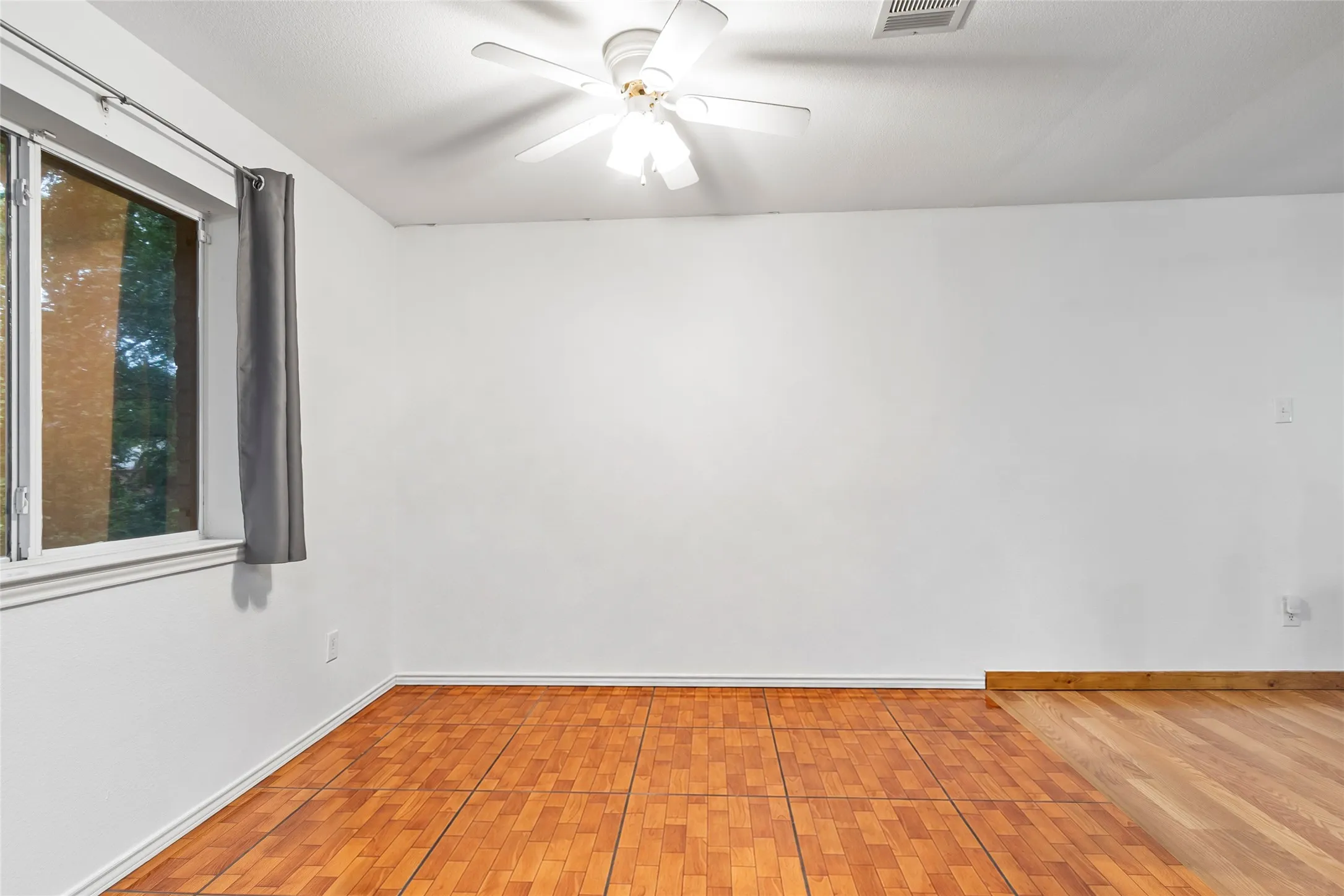 STAGE Rectangular window, wood-finish flooring, white walls, and a ceiling fan with integrated lighting
