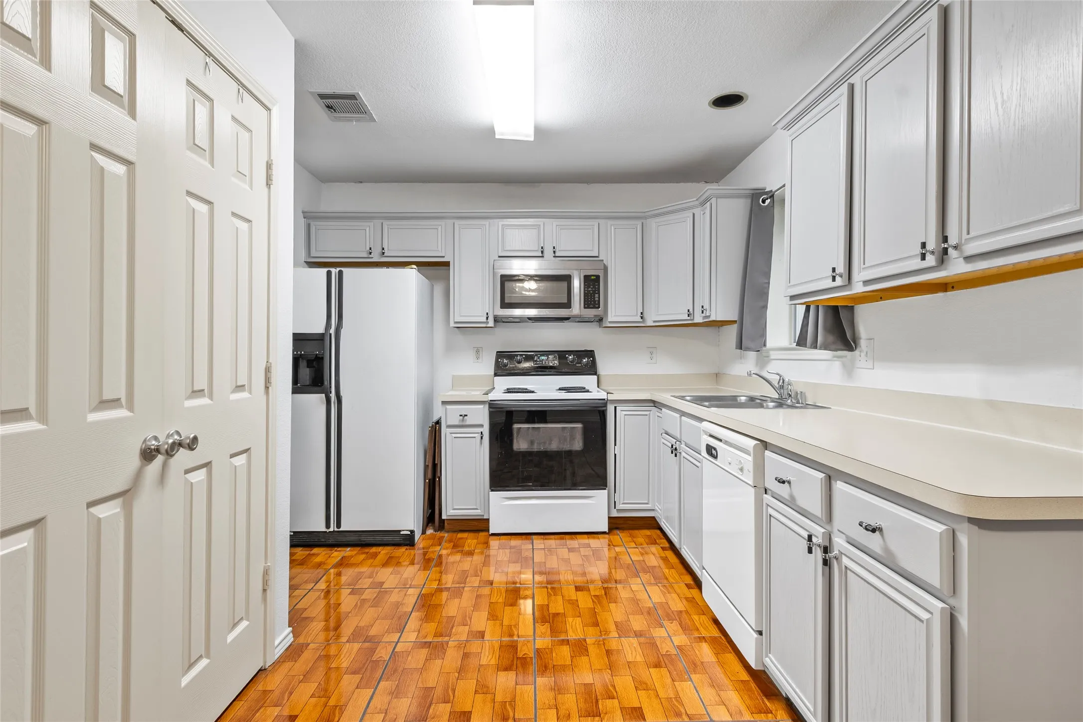 STAGE Kitchen featuring light-toned cabinetry, light-toned countertops, a stainless steel microwave, and wood-finish flooring
