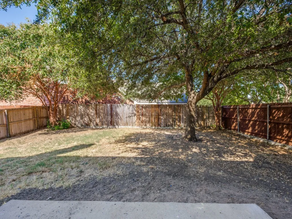 Private backyard featuring mature trees, a concrete patio, and varied wooden fencing