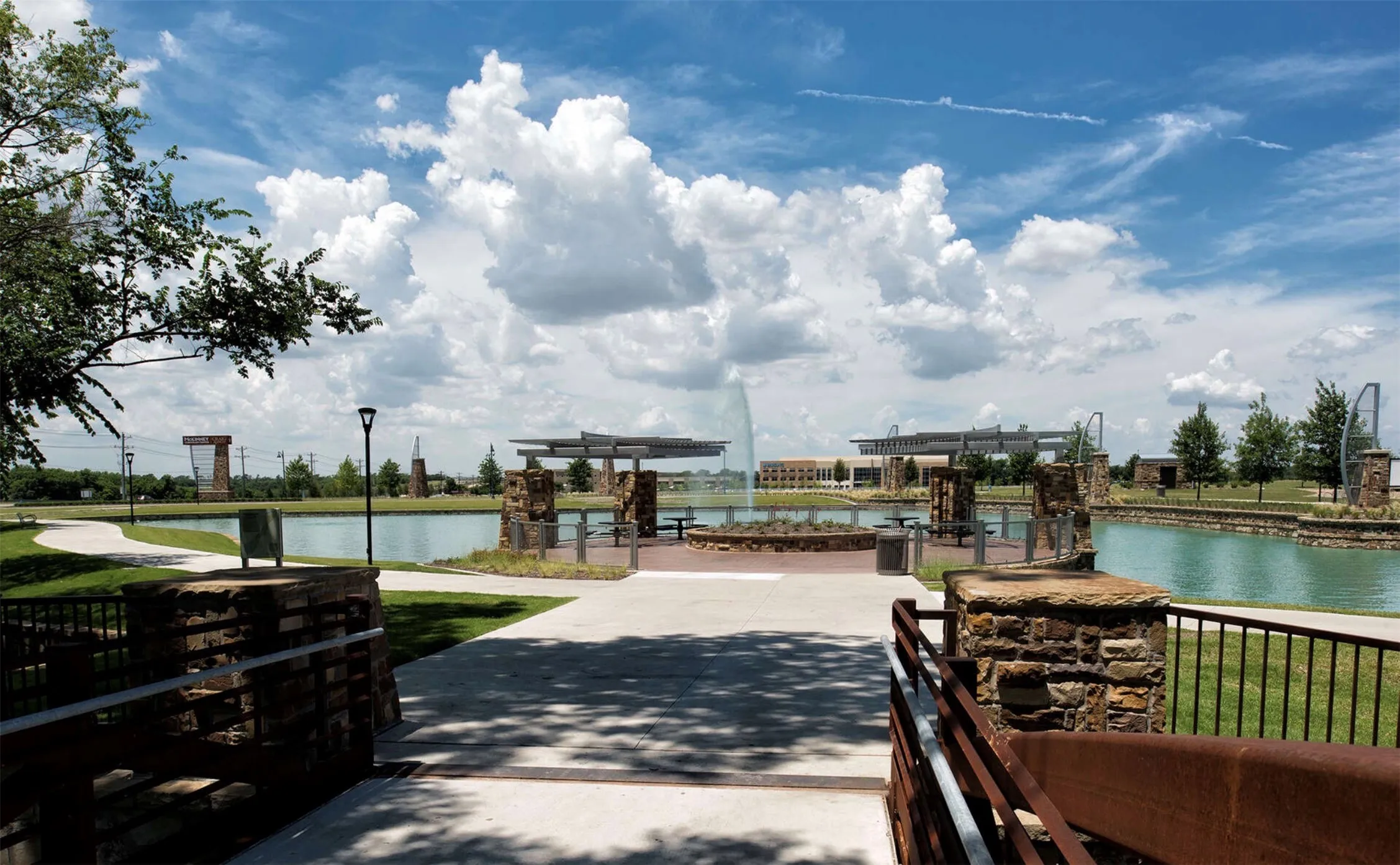 Paved walking paths, landscaped grounds, a serene pond with a water feature, a covered outdoor seating area, and stone-clad architectural elements