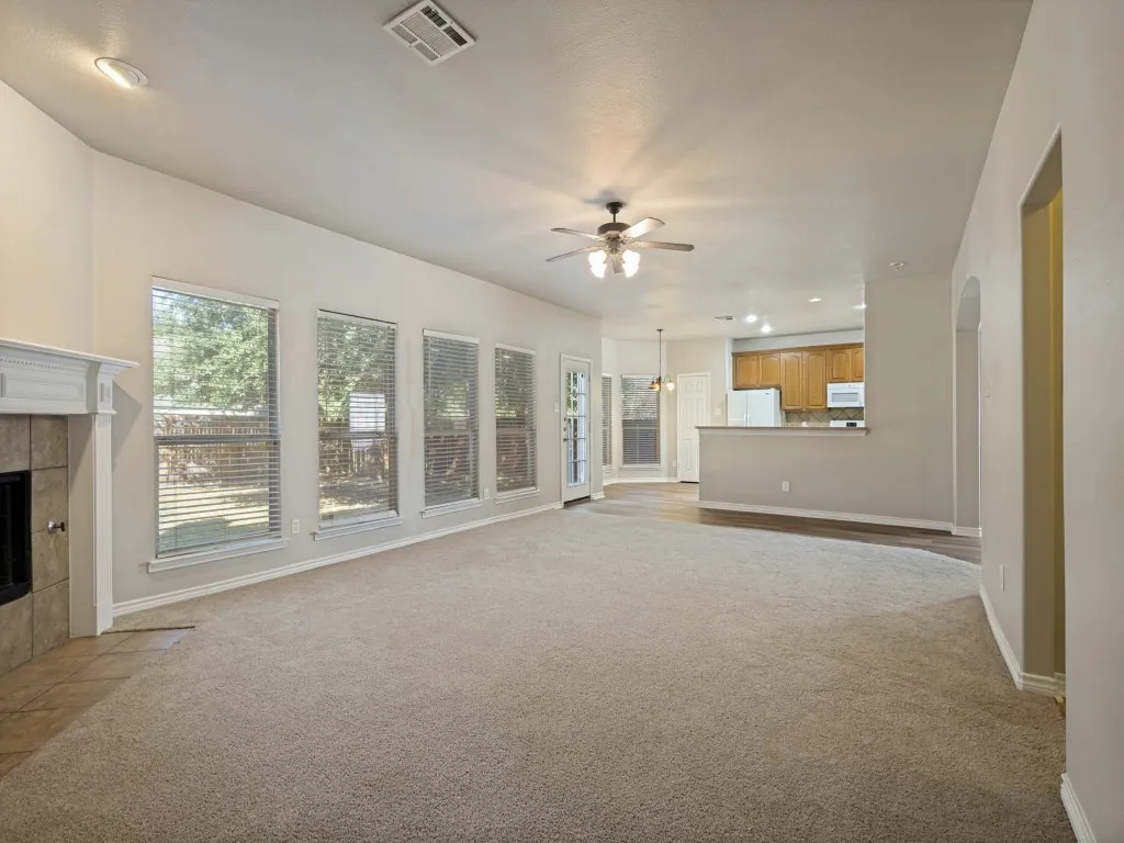 Spacious living area with neutral carpeting, a fireplace featuring a white mantel, The windows, the wall of windows brings natural light into the room