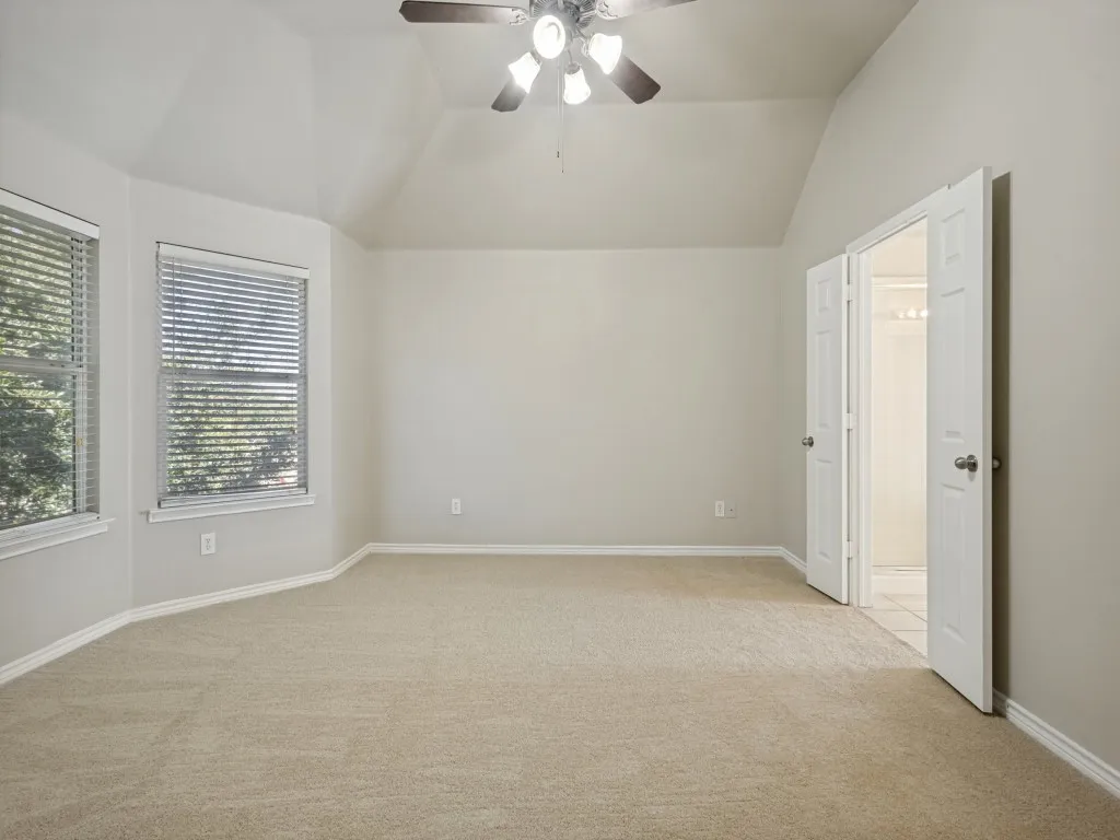 Vaulted ceiling with a ceiling fan, bay window with 2”blinds, and white paneled double doors