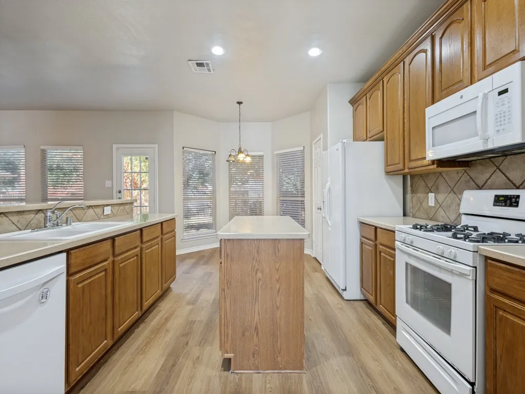 Kitchen featuring custom wood cabinetry, solid surface countertops, white appliances, and wood-laminatefinish flooring