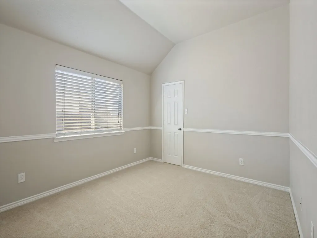 Vaulted ceiling, neutral tone walls, white trim details, window with blinds, and carpeted flooring