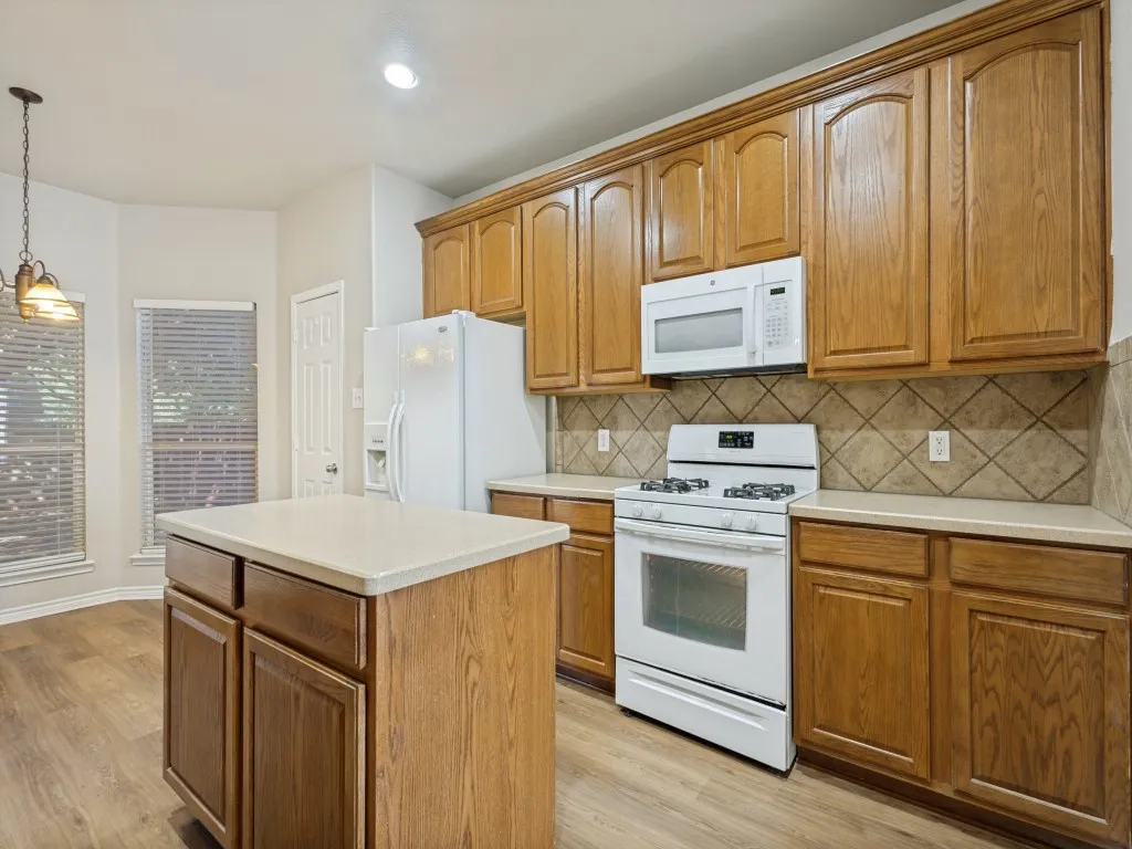 Kitchen featuring customwood-cabinetry, a central island, a white appliance package, and a tile backsplash