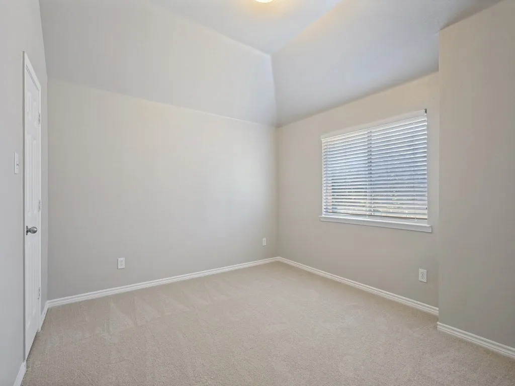 Vaulted ceiling, neutral wall paint, carpet flooring, window with blinds, and white trim