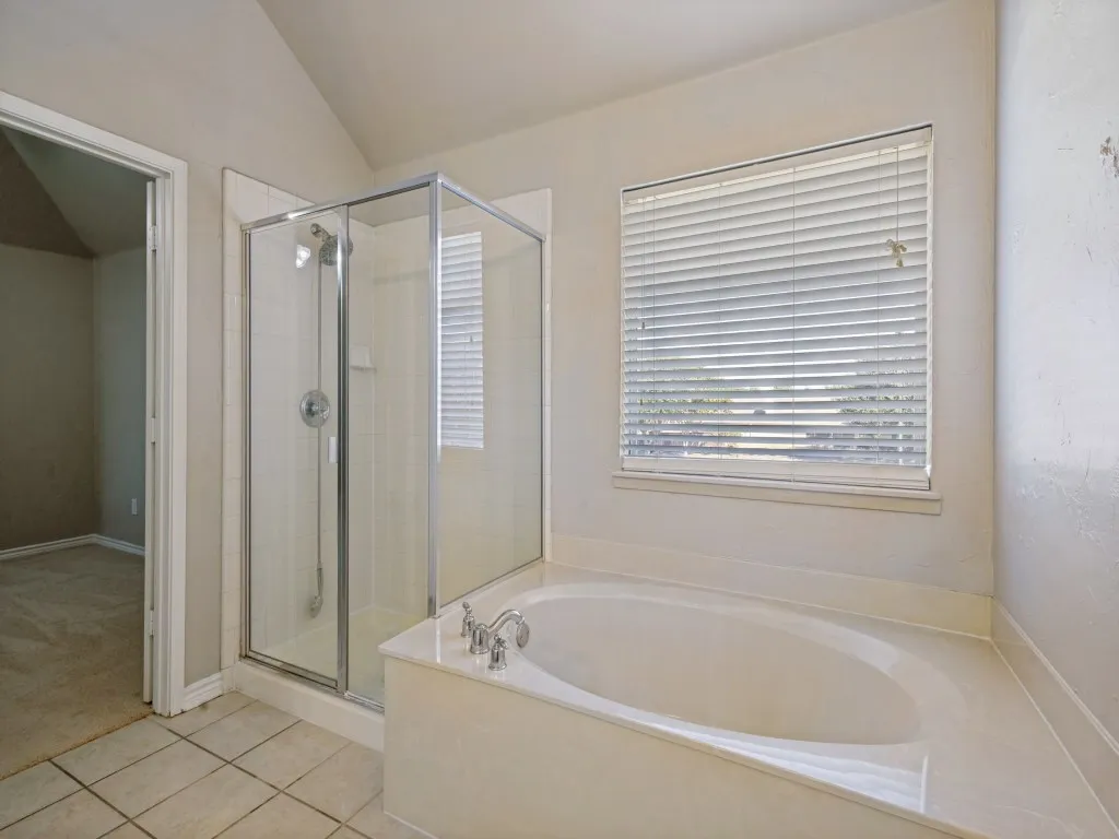 soaking tub, a separate glass-enclosed shower, tileflooring, and a large window