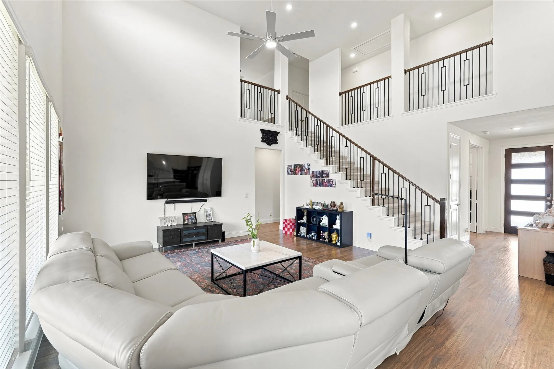 Two-story living area with high ceilings, wood-finish flooring, a contemporary staircase with metal balusters, and a modern entry door with horizontal lites