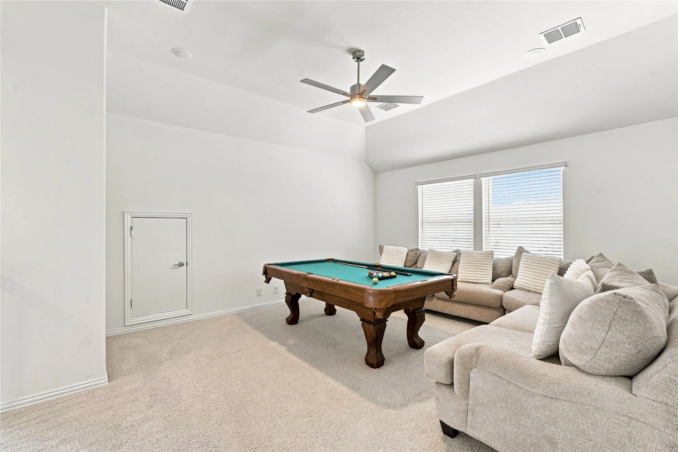 Vaulted ceiling, ceiling fan, carpet flooring, multiple windows with blinds, and a built-in door