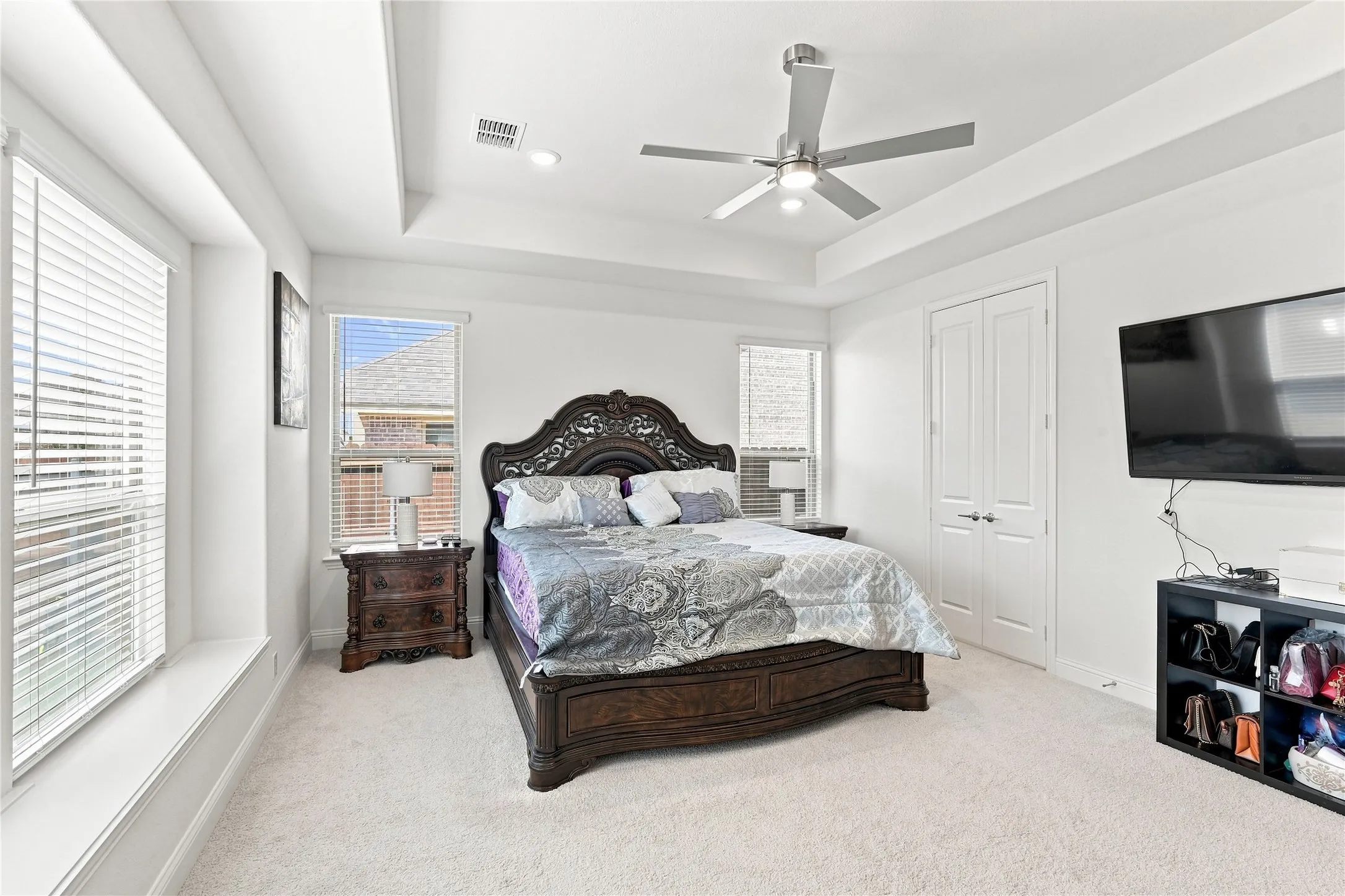 Tray ceiling with recessed lighting and a ceiling fan, dual windows with blinds, and light-toned carpeting
