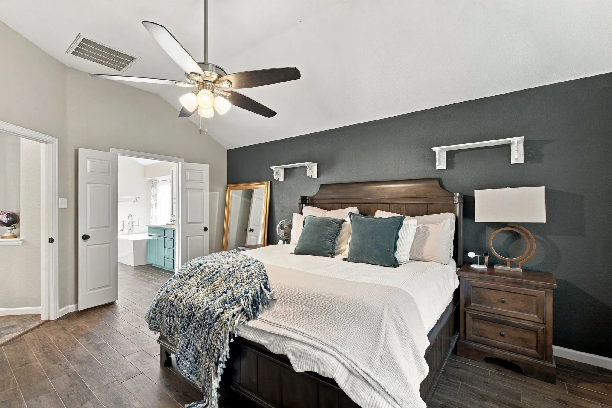 Vaulted ceiling with a ceiling fan, wood-finish flooring, shaker-style doors, and a dark accent wall