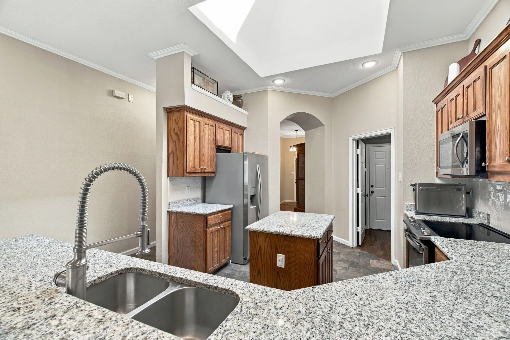 Kitchen featuring granite countertops, wood cabinetry, a double basin sink with a high-arc faucet, and an arched doorway