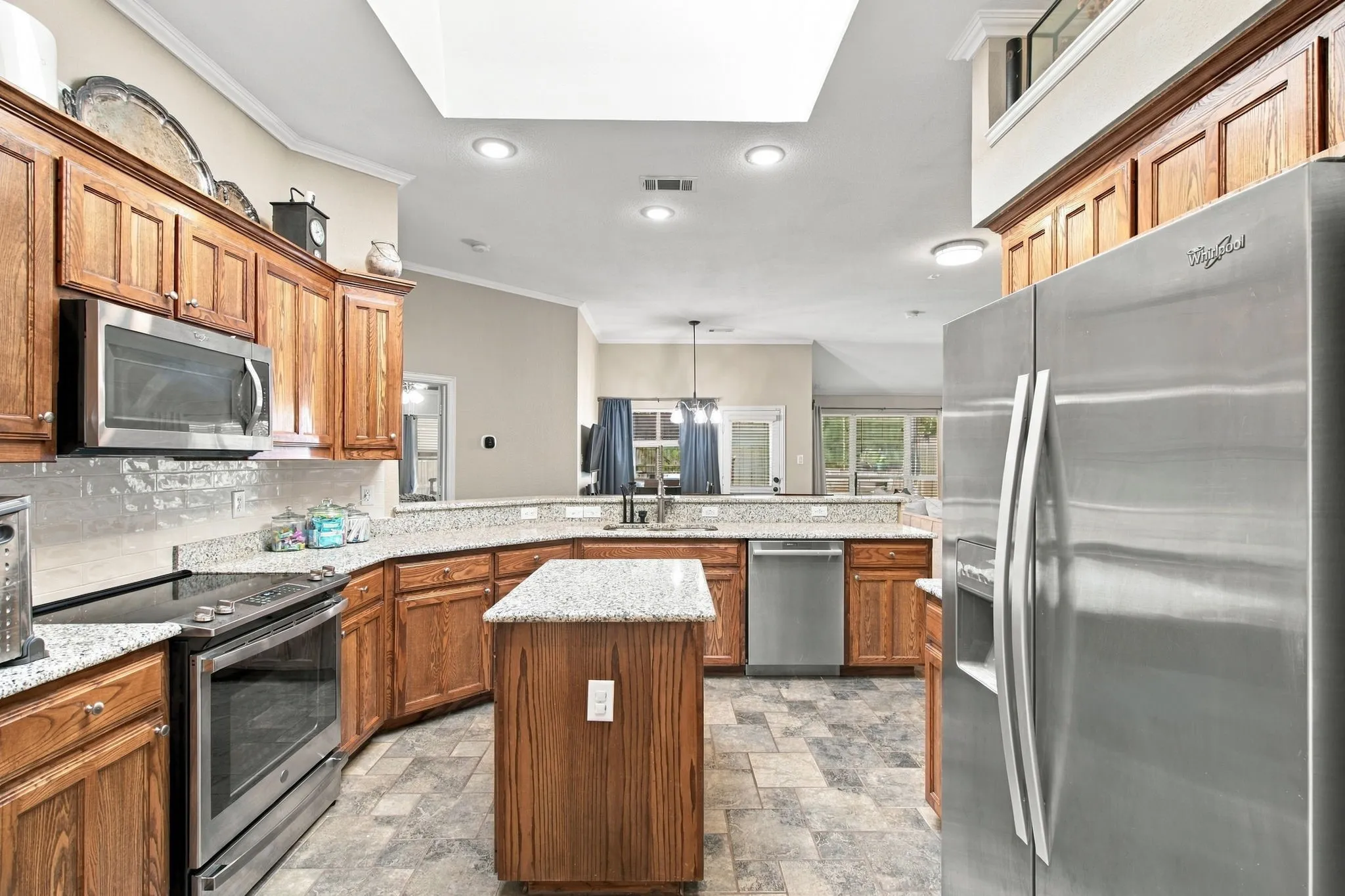 Spacious kitchen featuring wood cabinetry, stainless steel appliances, speckled countertops, a central island, and recessed lighting