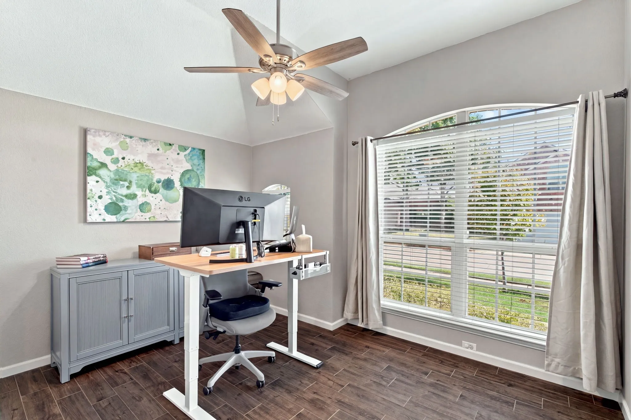 Vaulted ceiling with a ceiling fan, wood-finish flooring, a large arched window, and neutral wall tones