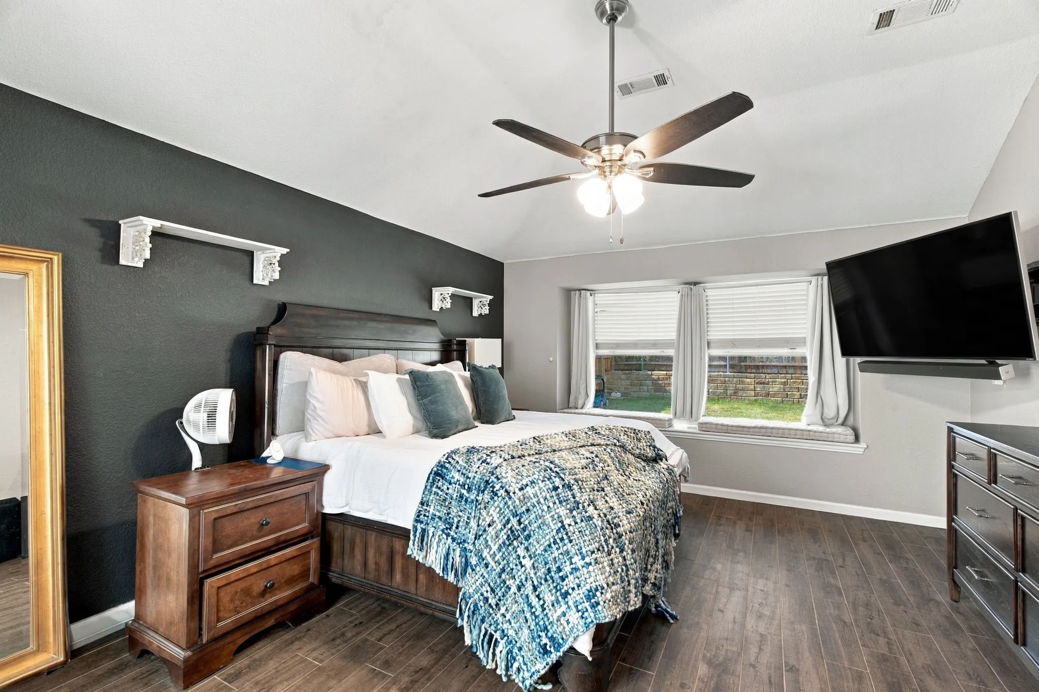 Vaulted ceiling with a ceiling fan, wood-finish flooring, accent wall, and window seating