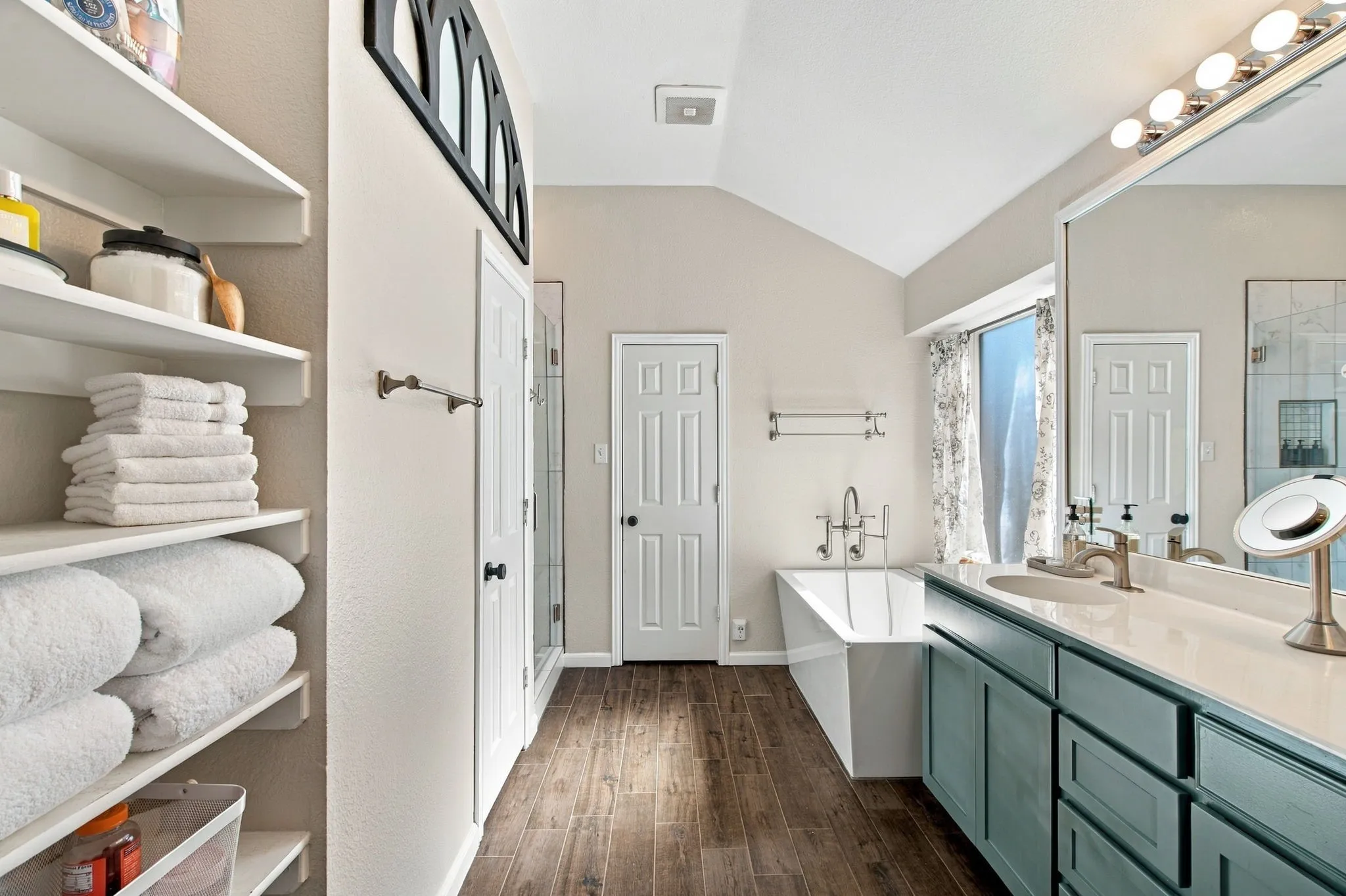 Vaulted ceiling, wood-finish flooring, built-in shelving, freestanding soaking tub, and a dual vanity with a large mirror