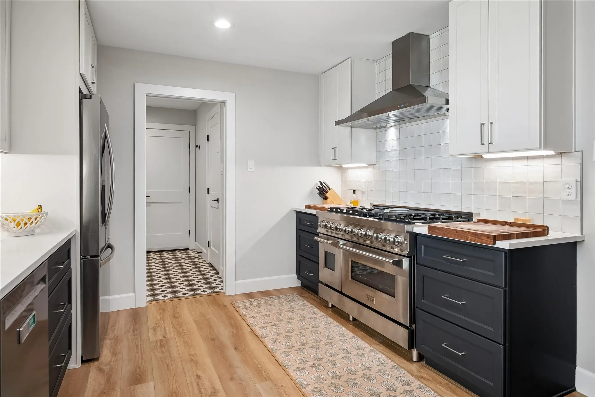 Modern kitchen with two-tone cabinetry, stainless steel range and hood, white countertops, and wood-finish flooring
