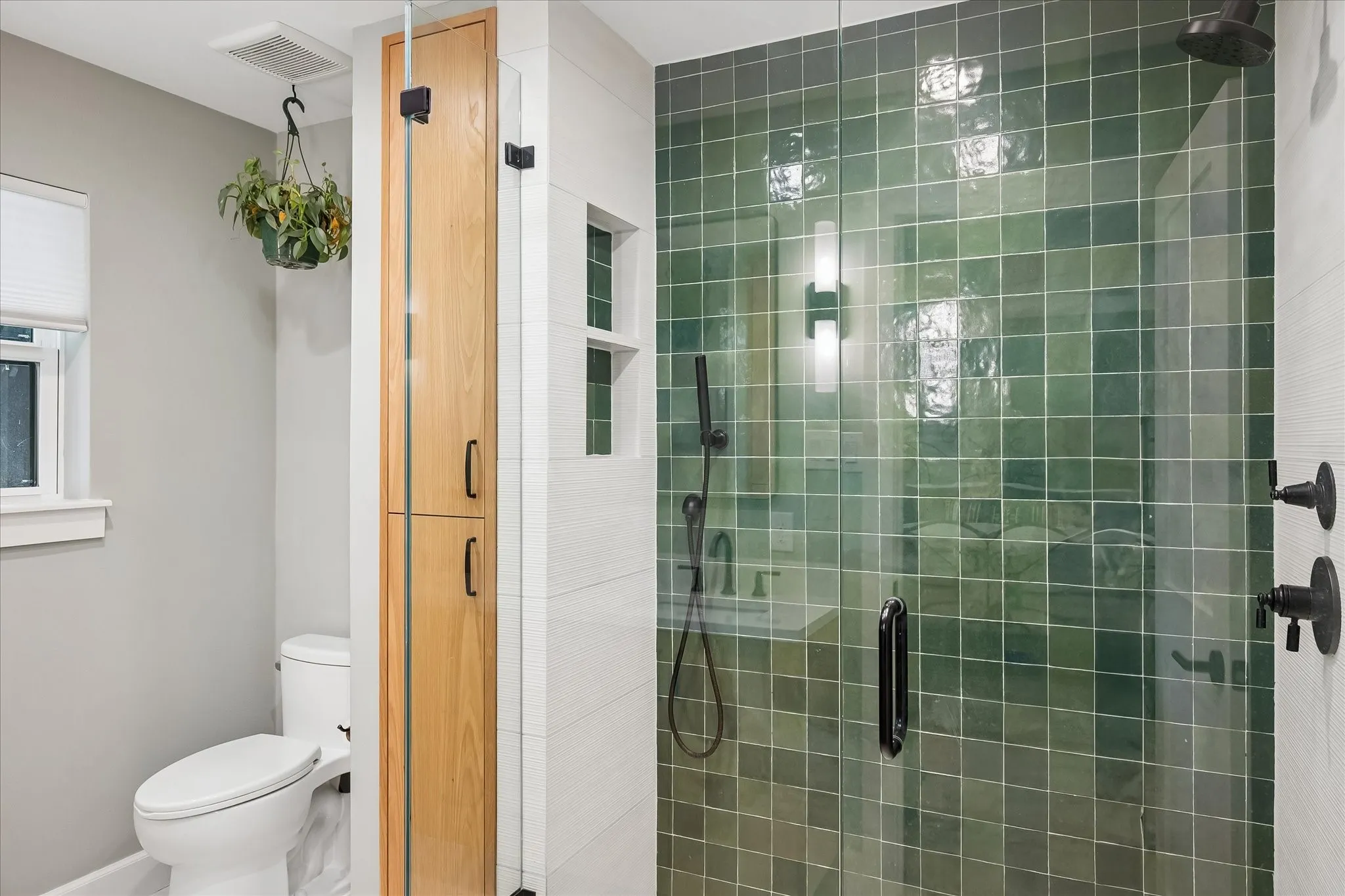 Custom shower enclosure with green tile surround, wood-finish built-in storage cabinetry, and matte black shower fixtures