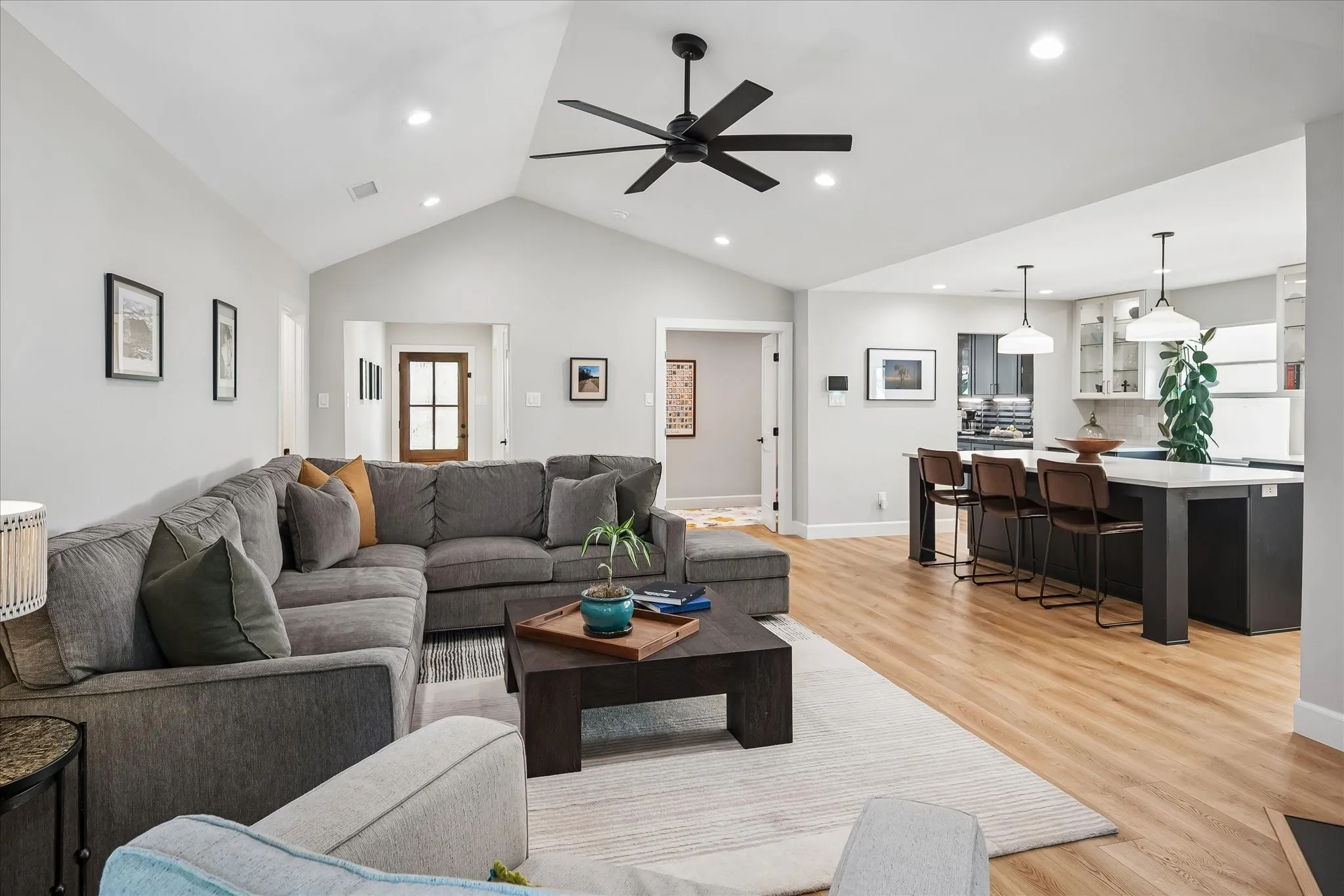 Vaulted ceiling with a ceiling fan and recessed lighting, wood-finish flooring, kitchen island with seating, and pendant lighting over the kitchen island
