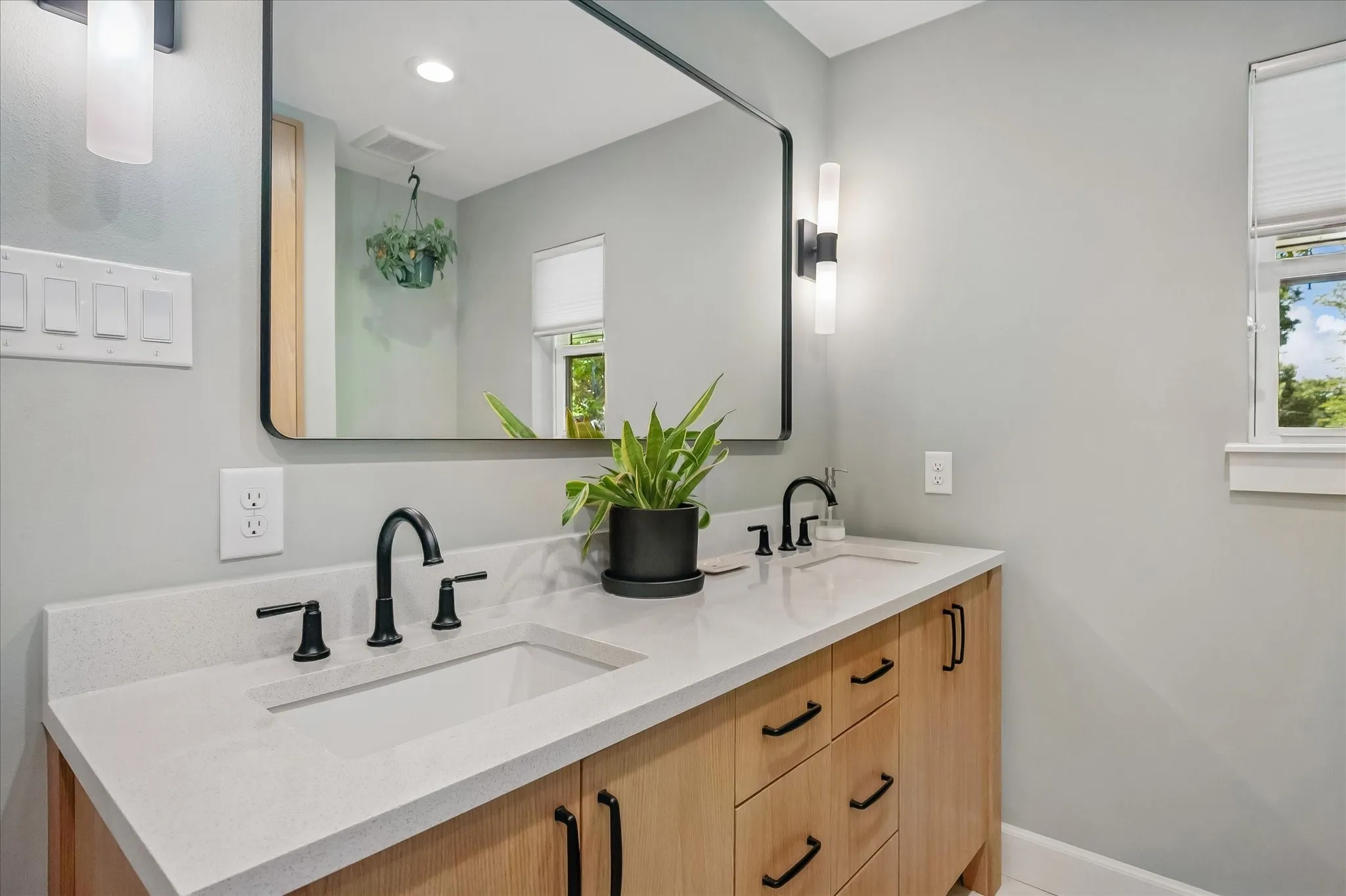 Dual vanity with integrated sinks, light-toned wood-finish cabinetry, black hardware, and a black-framed mirror