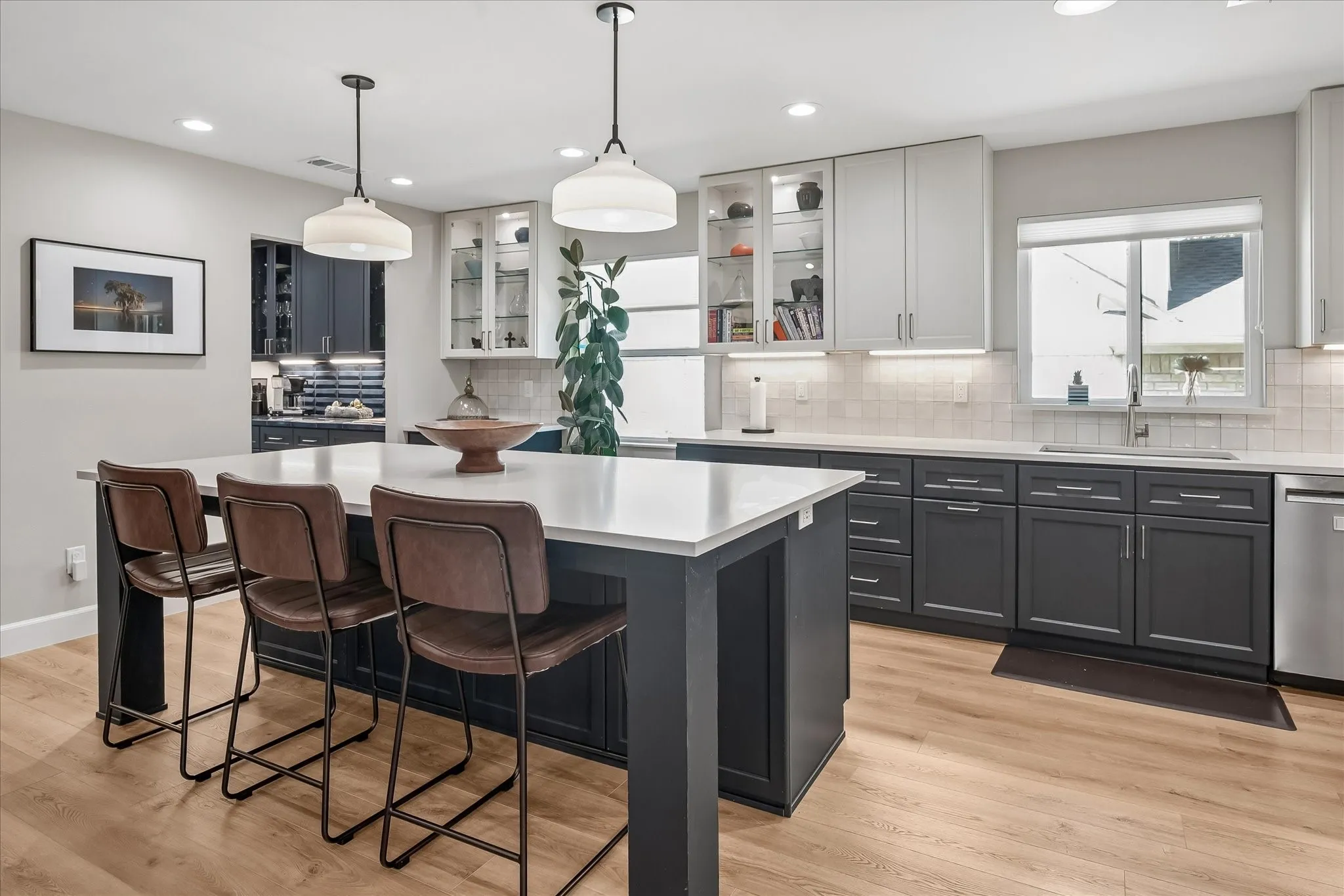 Spacious kitchen featuring an expansive island with seating, pendant lighting, two-tone cabinetry, wood-finish flooring, and a large window