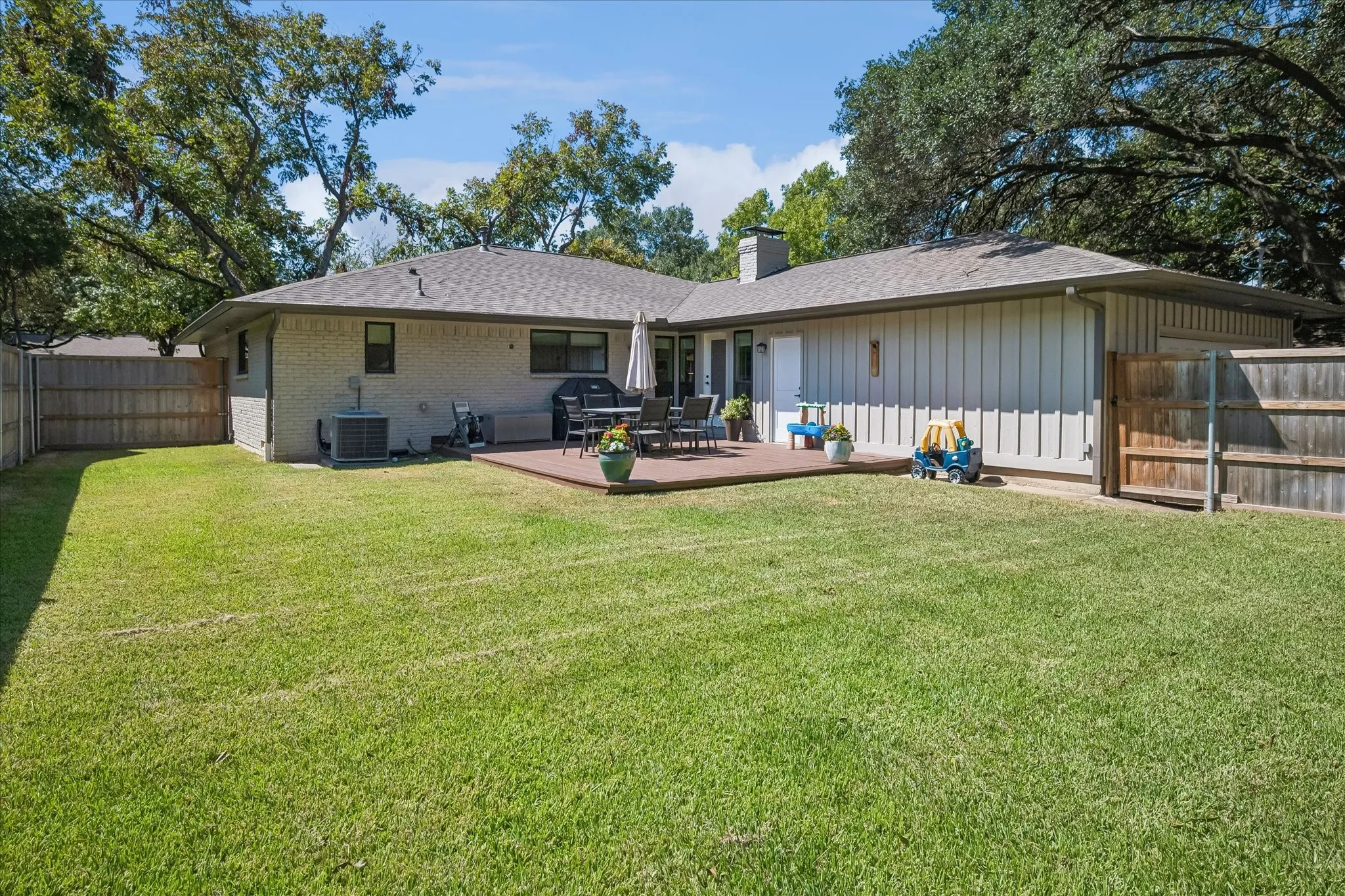 Expansive green lawn, a wooden privacy fence, and mature trees