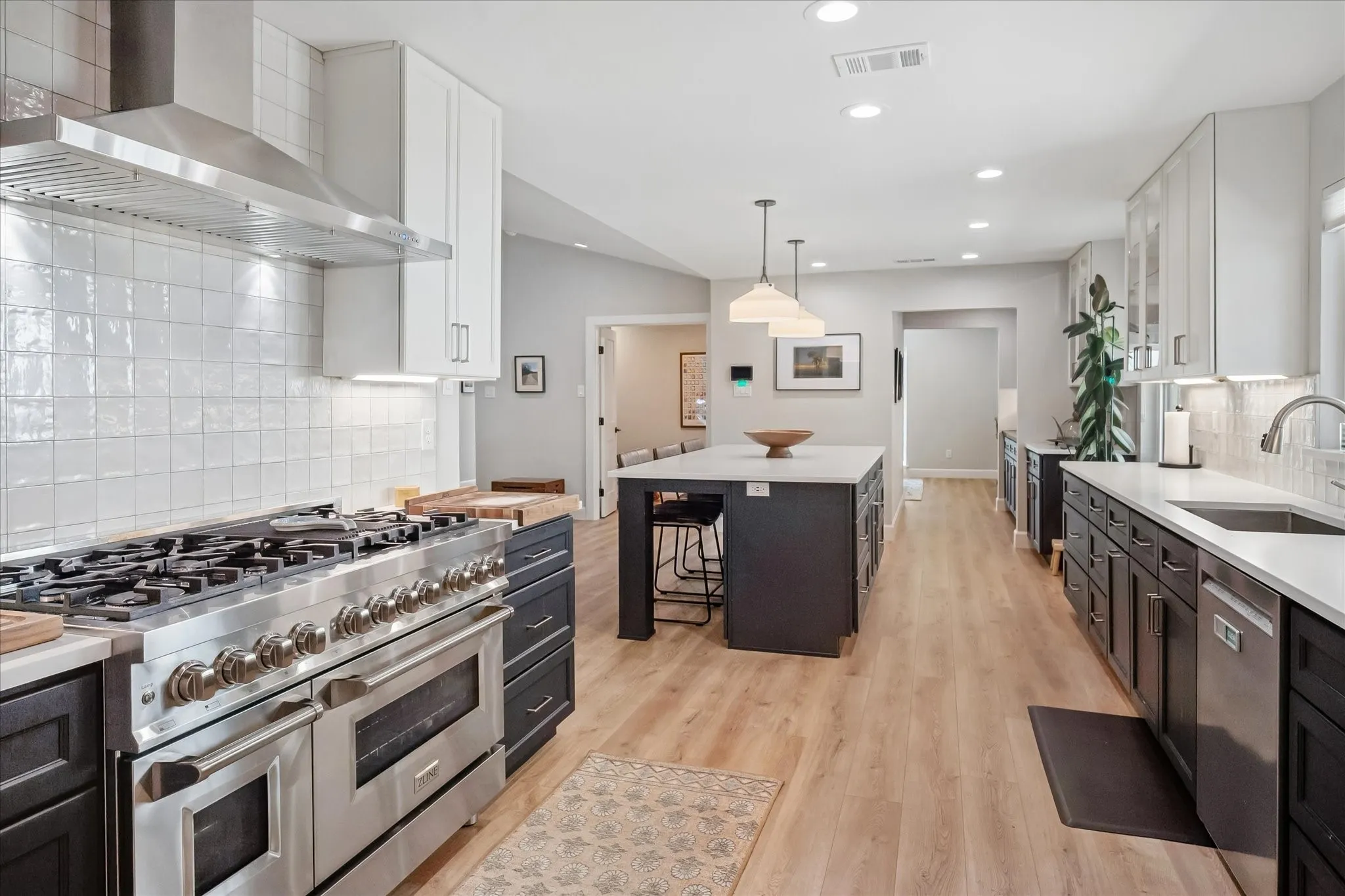 Spacious kitchen featuring wood-finish flooring, a large kitchen island with seating, dark lower cabinetry, light upper cabinetry, and a stainless steel professional-grade range with a matching vent hood