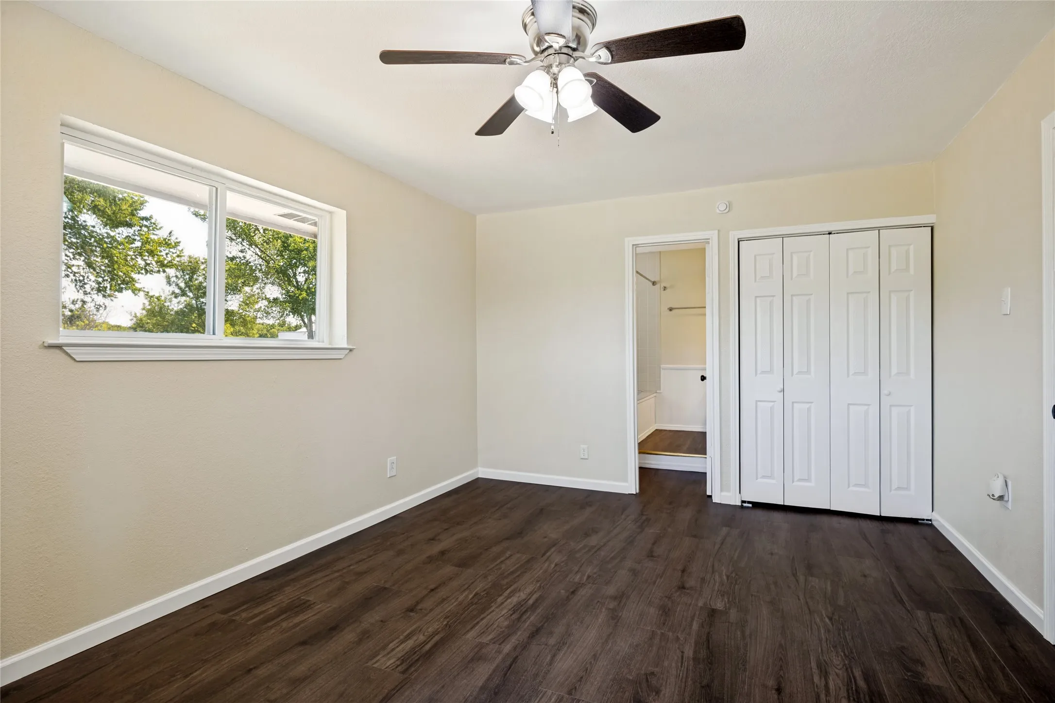 Wood-finish flooring, bright window, ceiling fan with light, bi-fold closet doors, and light-toned wall paint