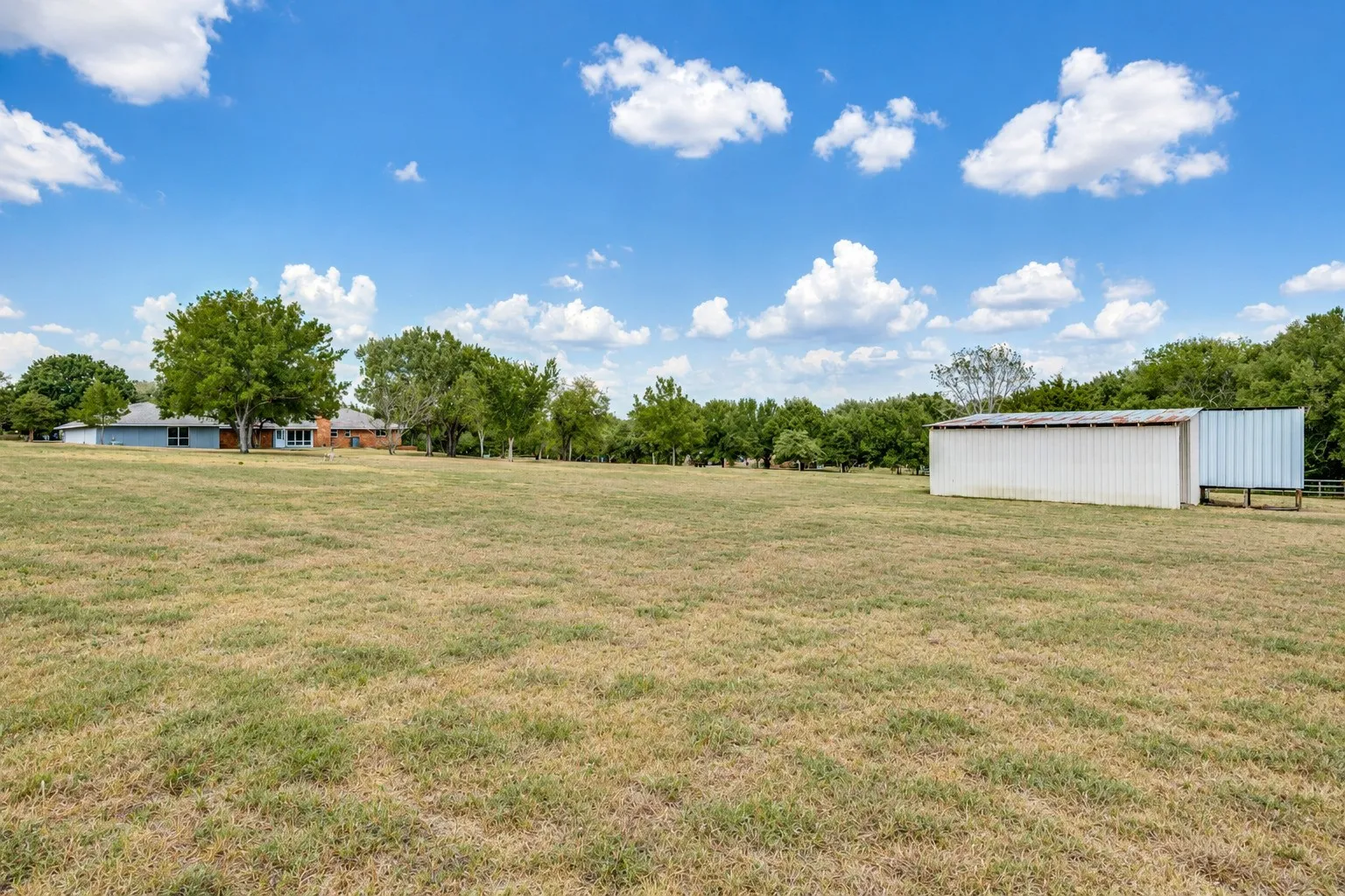 Expansive grassy area featuring a white metal outbuilding and mature trees